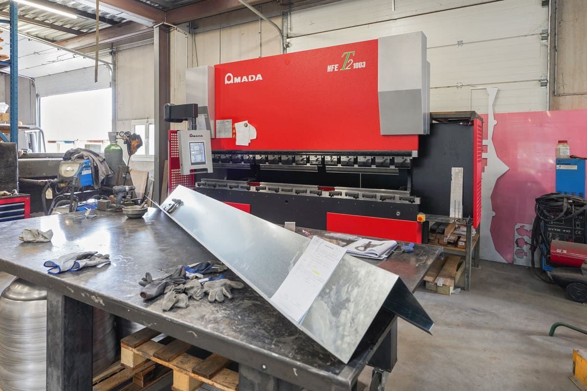 Presse plieuse industrielle rouge dans un atelier, en train de plier une grande tôle.