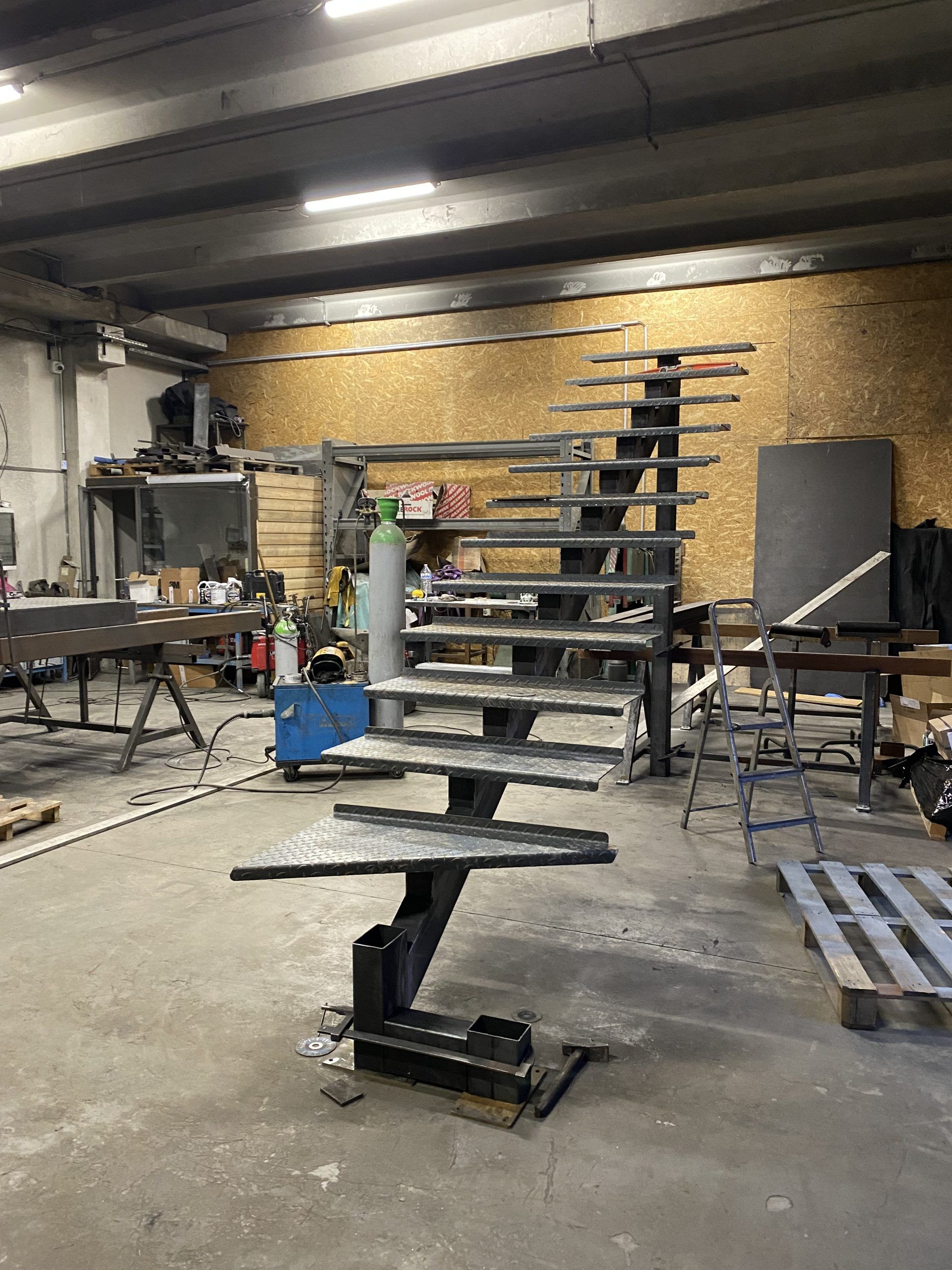 Atelier industriel avec un empilement de cadres métalliques et d'étagères dans un espace encombré ressemblant à un garage