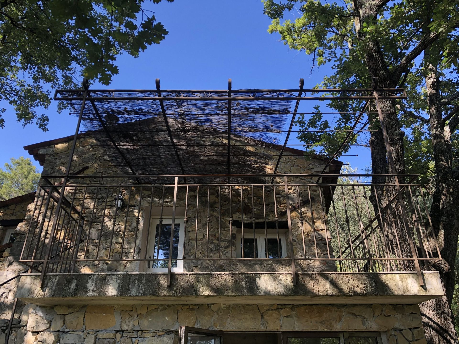 Façade d'une vieille maison en pierre au toit sombre, partiellement recouverte d'échafaudages et encadrée par des arbres.