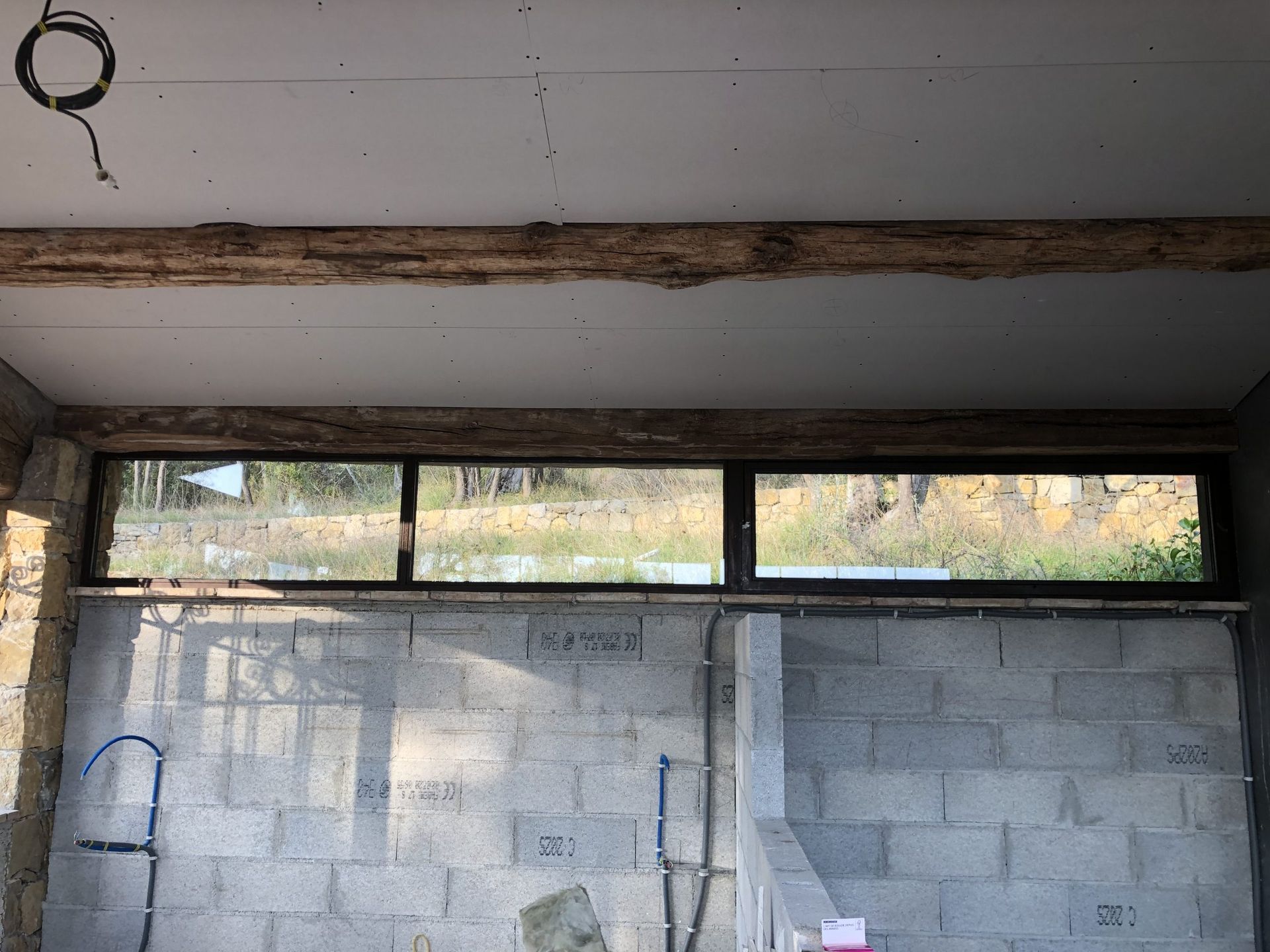 Mur en béton partiellement fini sous un plafond, avec des fenêtres étroites en partie supérieure et des débris de construction en partie inférieure.
