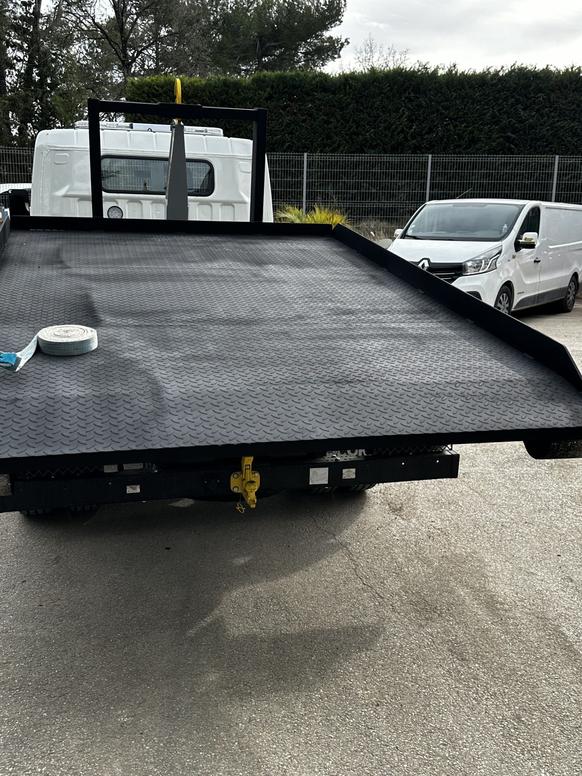 Un camion de dépannage noir à plateau charge une camionnette blanche sur un parking