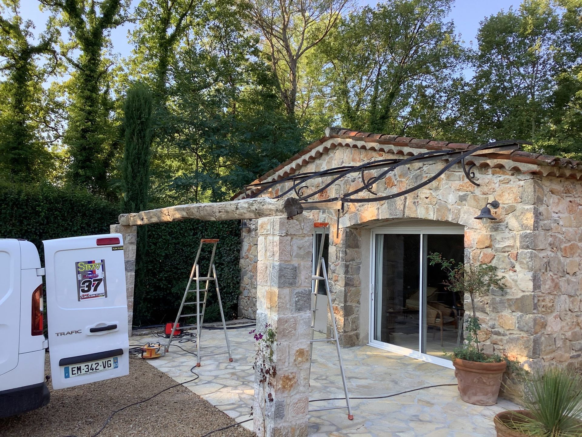 Maison en pierre en rénovation : porte coulissante ouverte, échafaudages et matériaux de construction à l’extérieur.