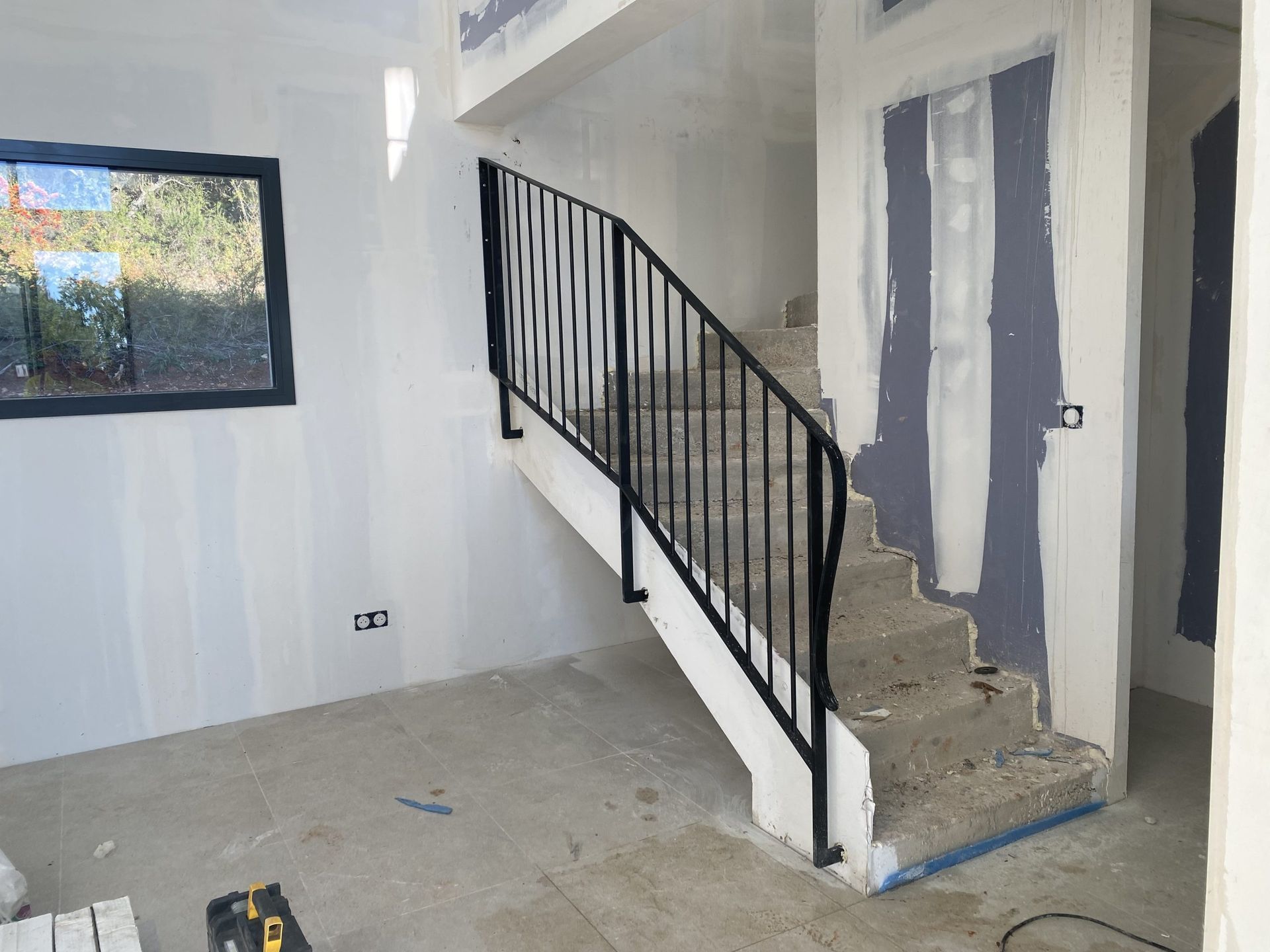 Intérieur en rénovation avec escalier, rampe noire, cloisons sèches non finies et une fenêtre