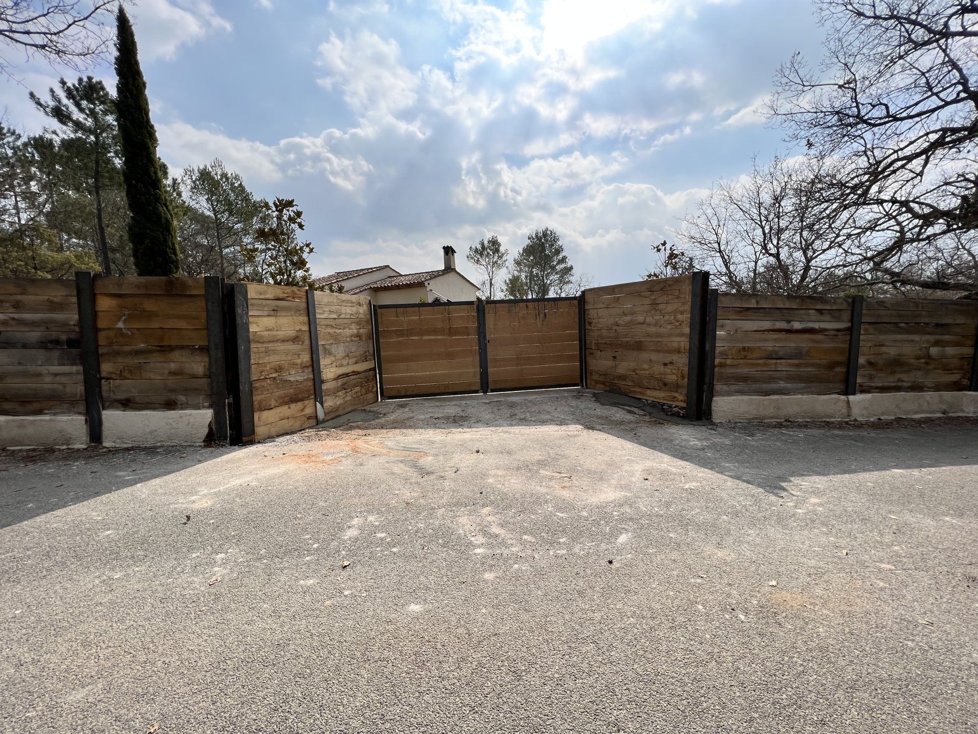 Allée de gravier menant à un portail et une clôture en bois sous un ciel nuageux