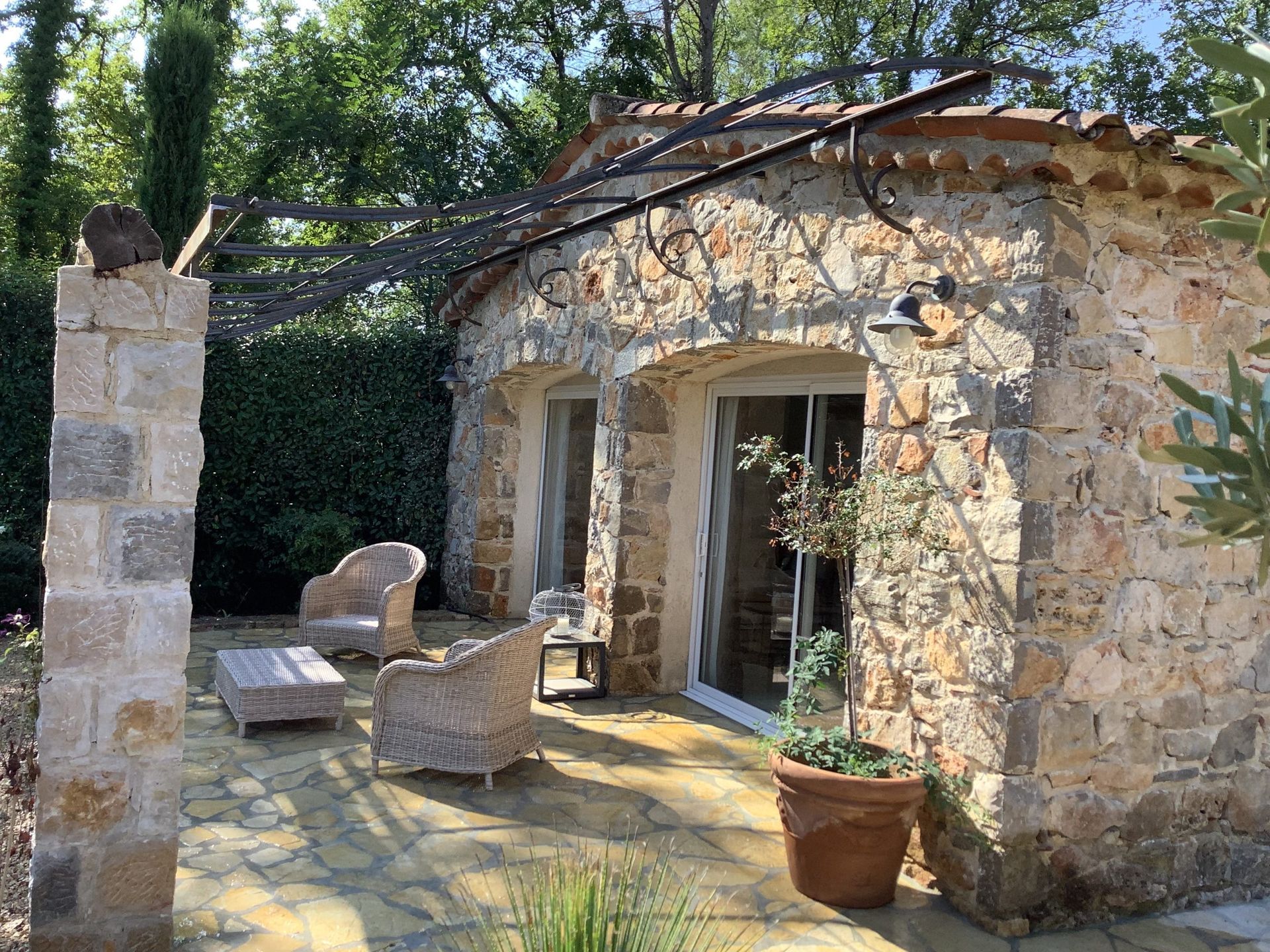 Patio rustique en pierre avec porte ouverte, plante en pot et cour ensoleillée avec chaises et table