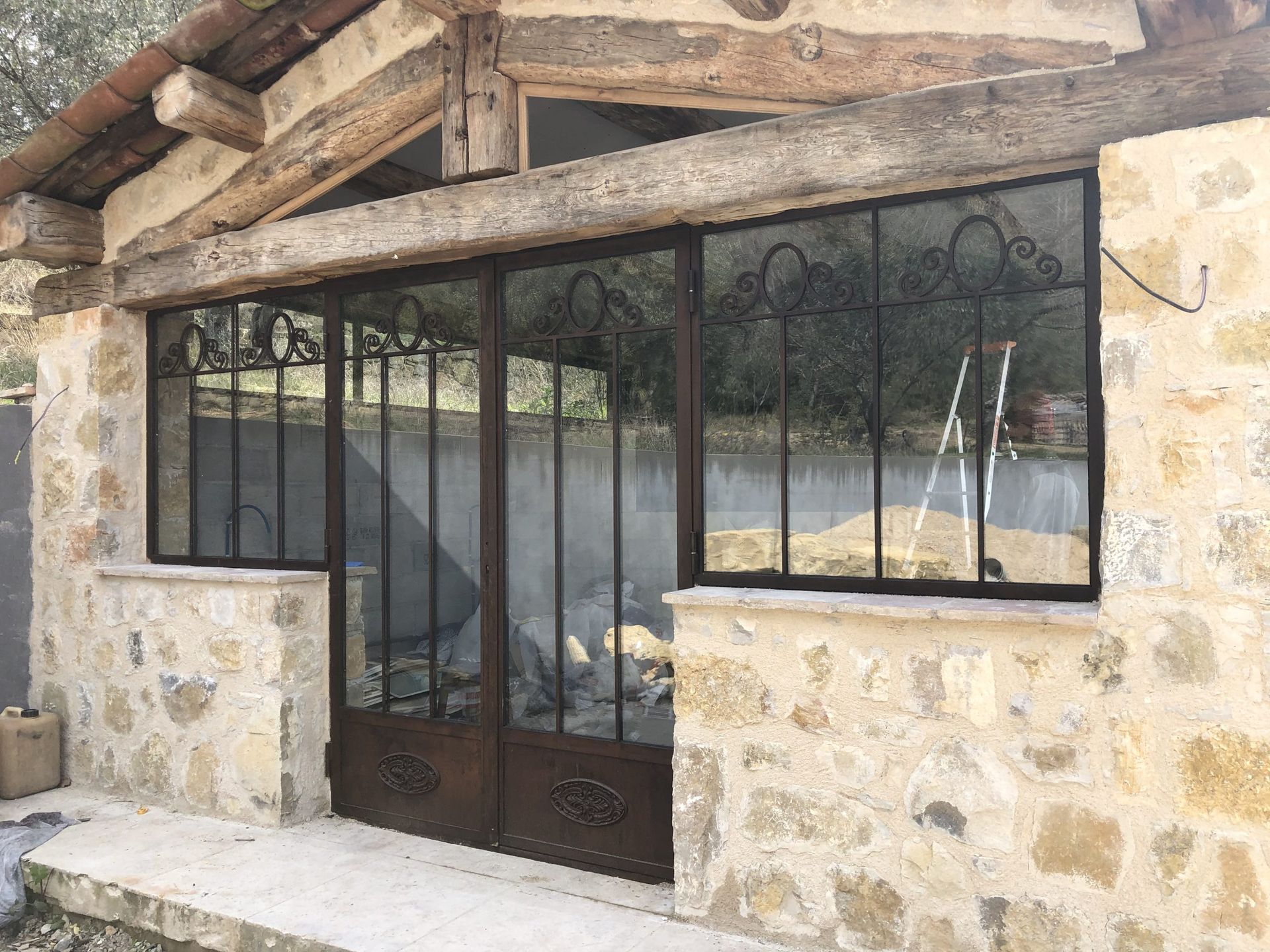 Entrée d'un bâtiment en pierre avec des barreaux en métal noir et un auvent en bois.
