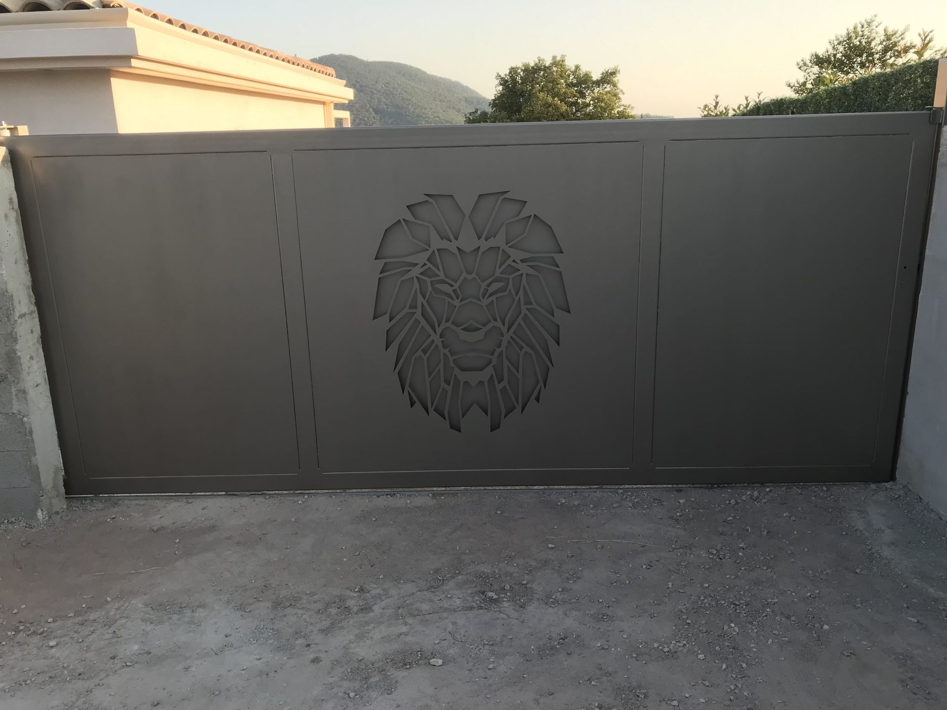 Portail en métal gris orné d'un lion, installé dans une allée bordée d'un mur blanc.
