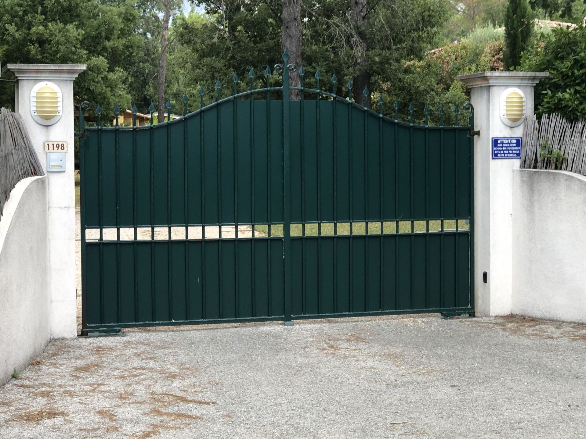 Portail métallique vert entre des piliers blancs à l'entrée d'une allée.