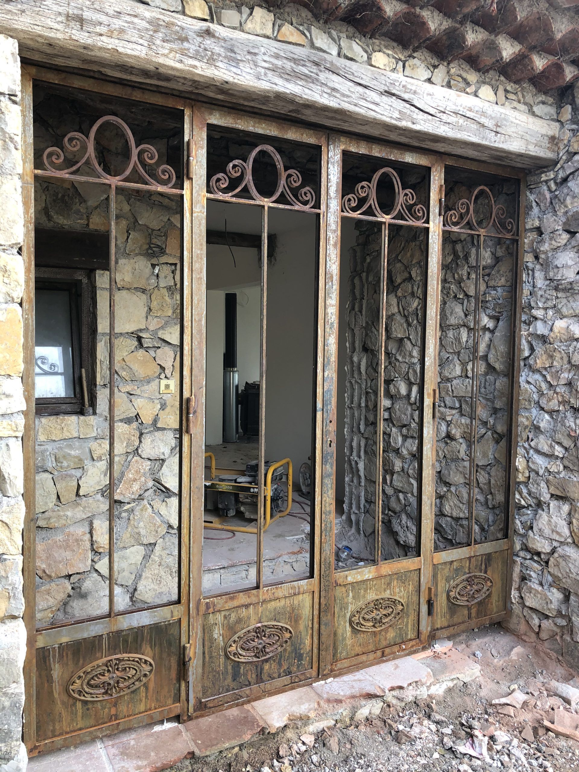 Double porte en métal rouillé et en verre sur un bâtiment en pierre délavée, laissant apparaître l'intérieur à travers les vitres.