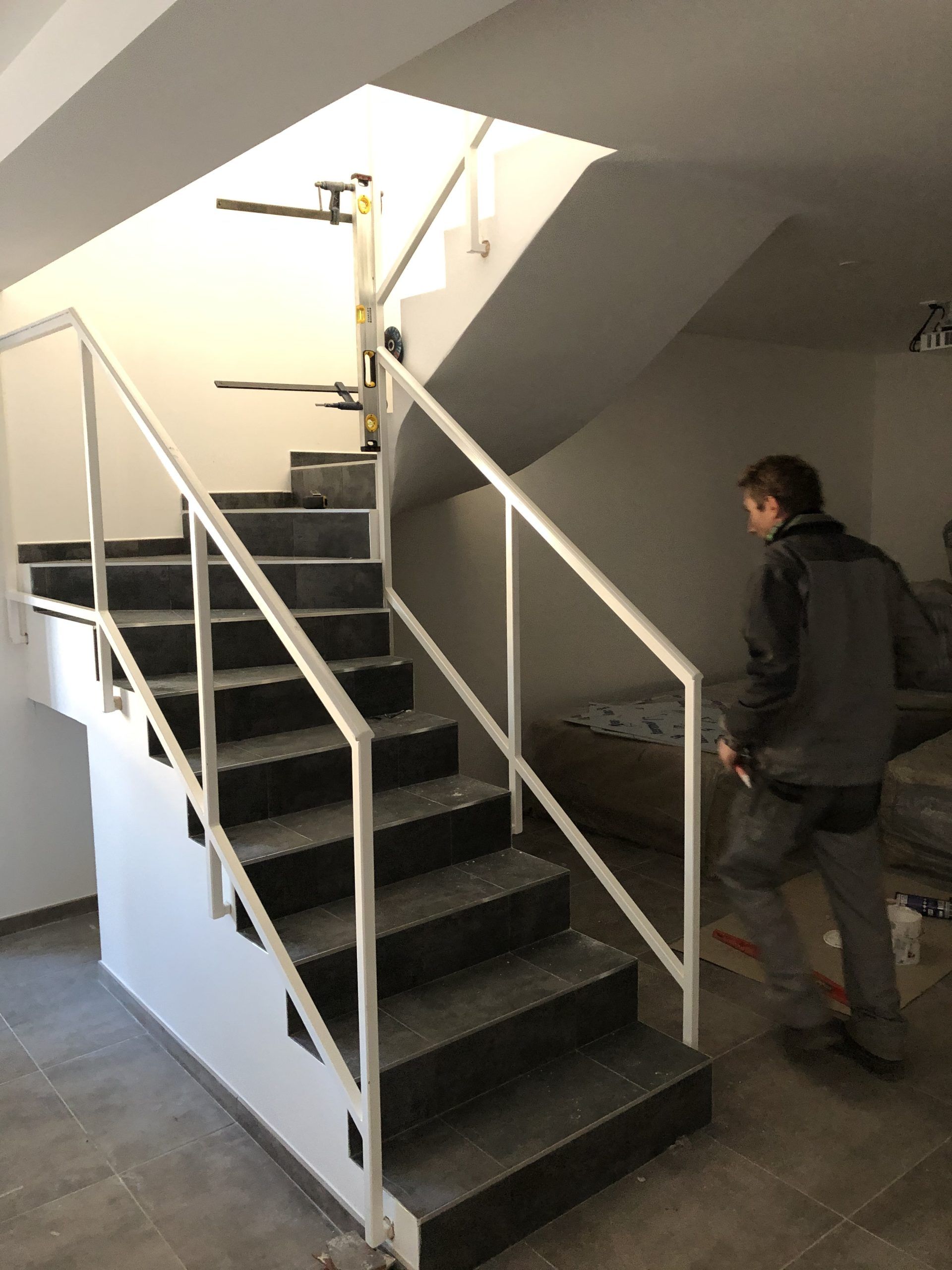 Escalier intérieur avec marches noires, rampes blanches et une personne montant les marches.