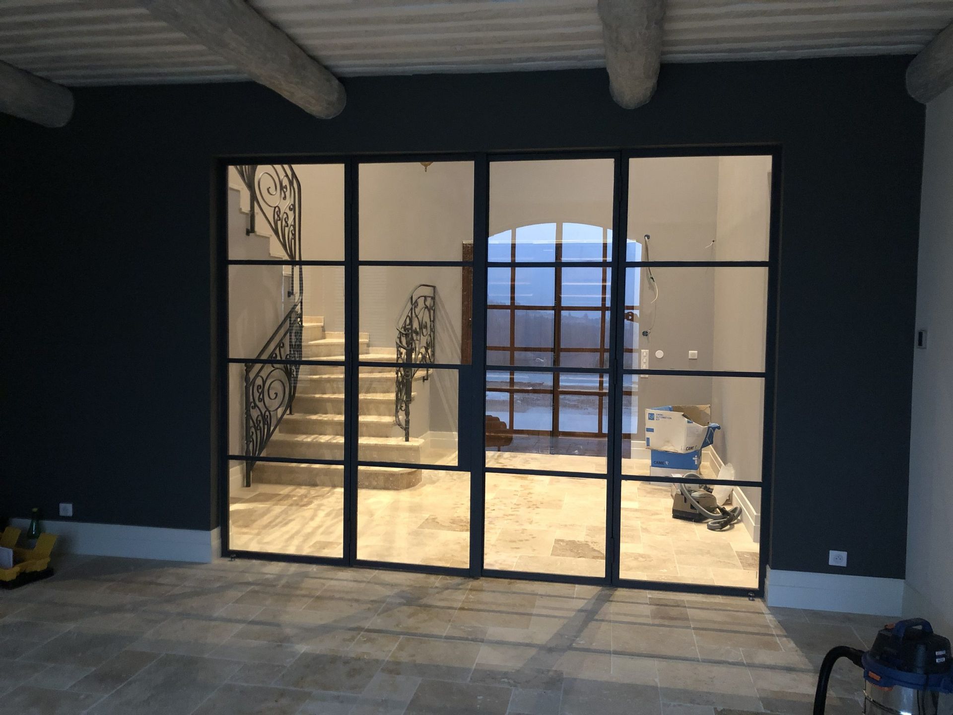 Intérieur moderne avec portes vitrées à cadre noir s'ouvrant sur un patio ensoleillé en construction