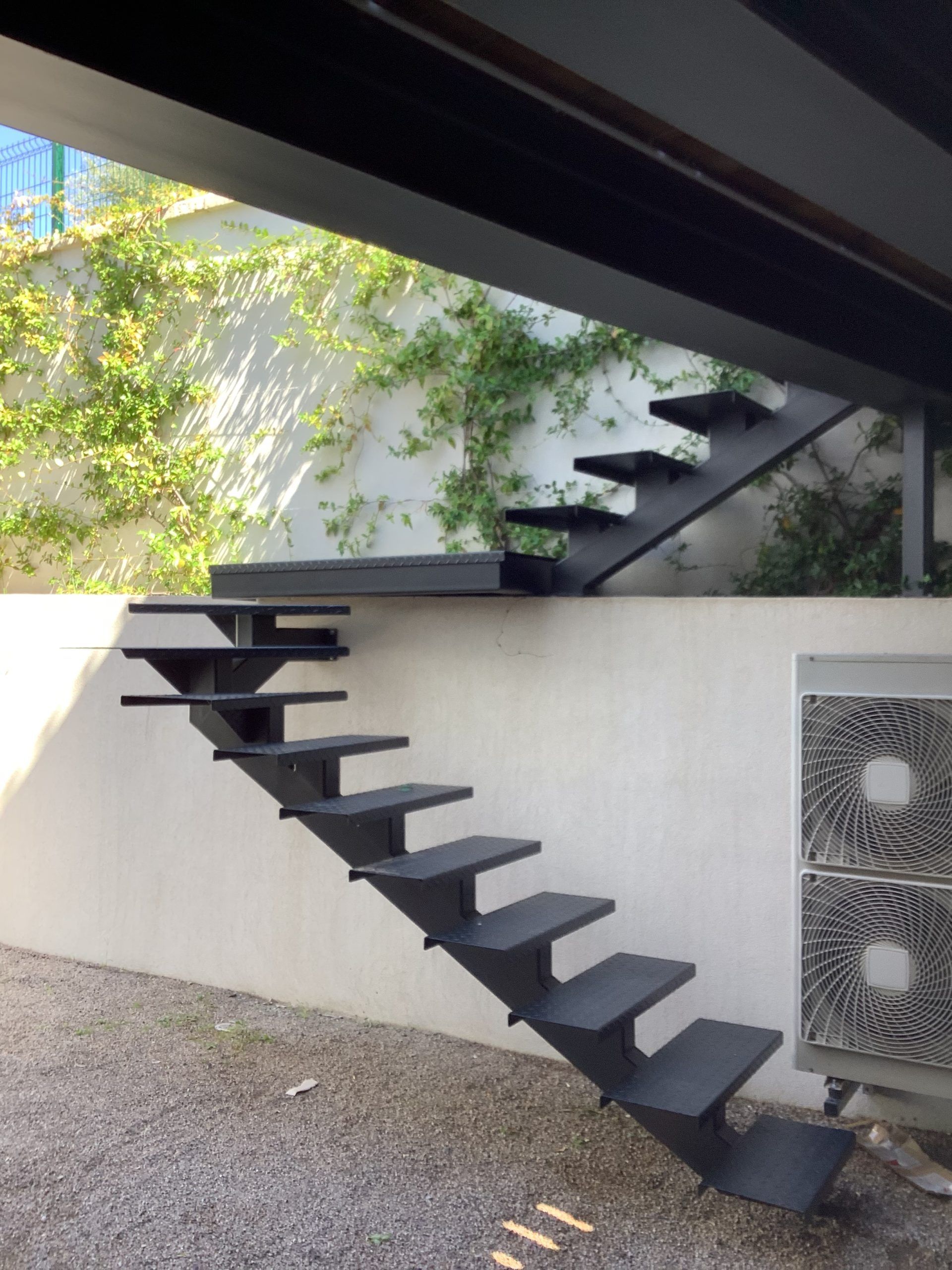 Escalier flottant noir moderne avec marches murales dans une cour extérieure