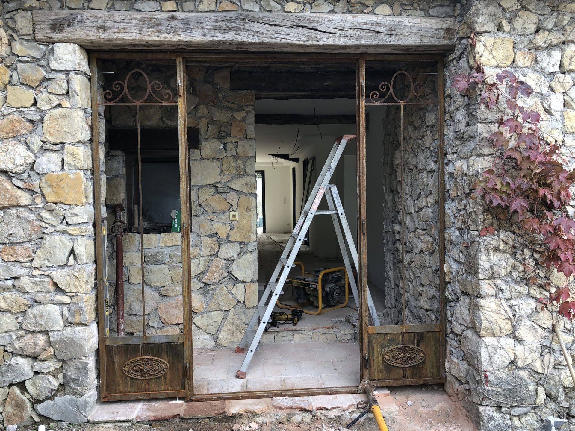 Porte en pierre avec grille métallique rouillée, échelle et intérieur inachevé d'un bâtiment en rénovation