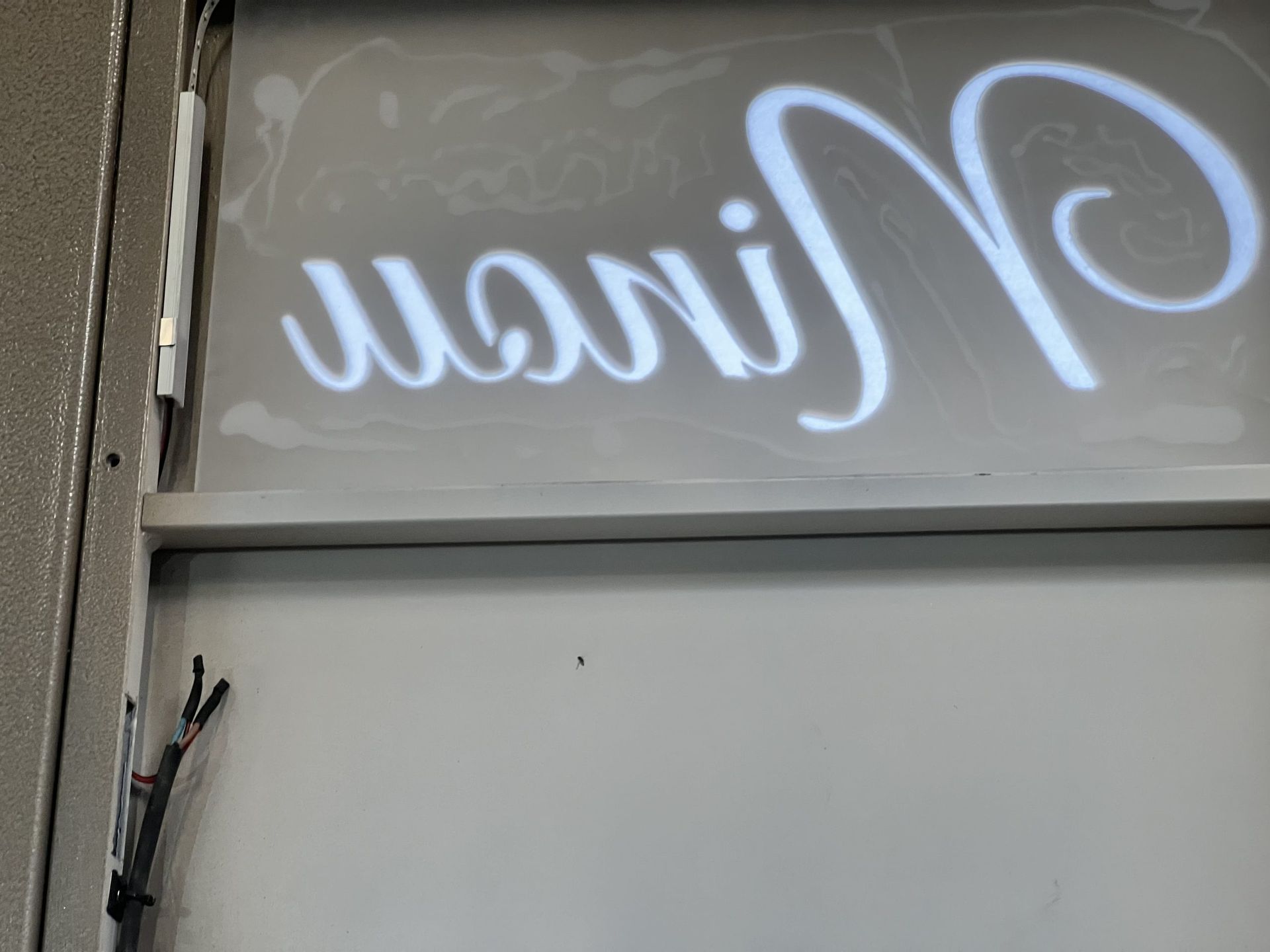 Enseigne illuminée dans la vitrine d'un magasin au-dessus d'un mur gris.