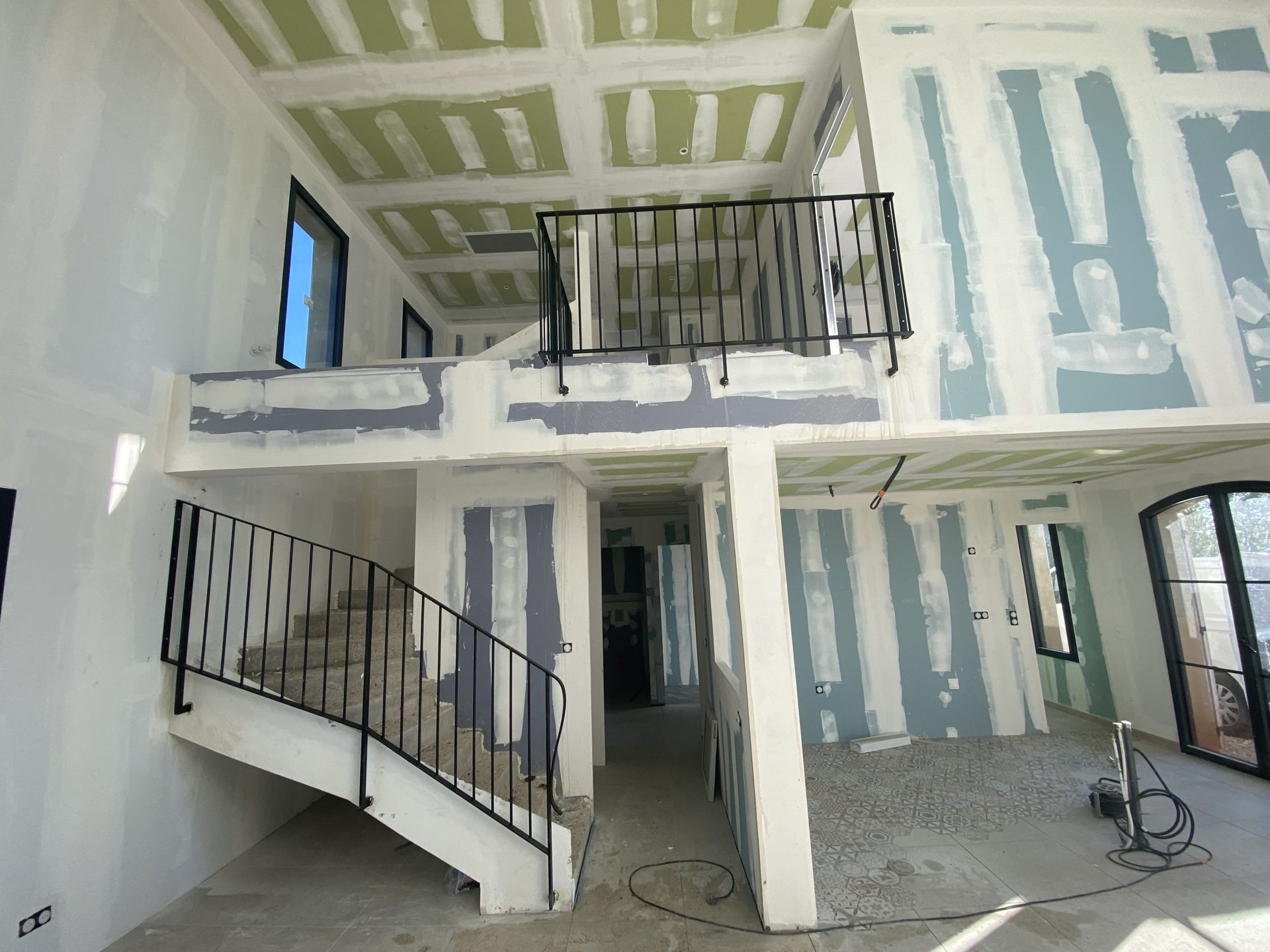 Intérieur d'une maison en construction avec cloisons sèches, escalier, balcon et charpente apparente.