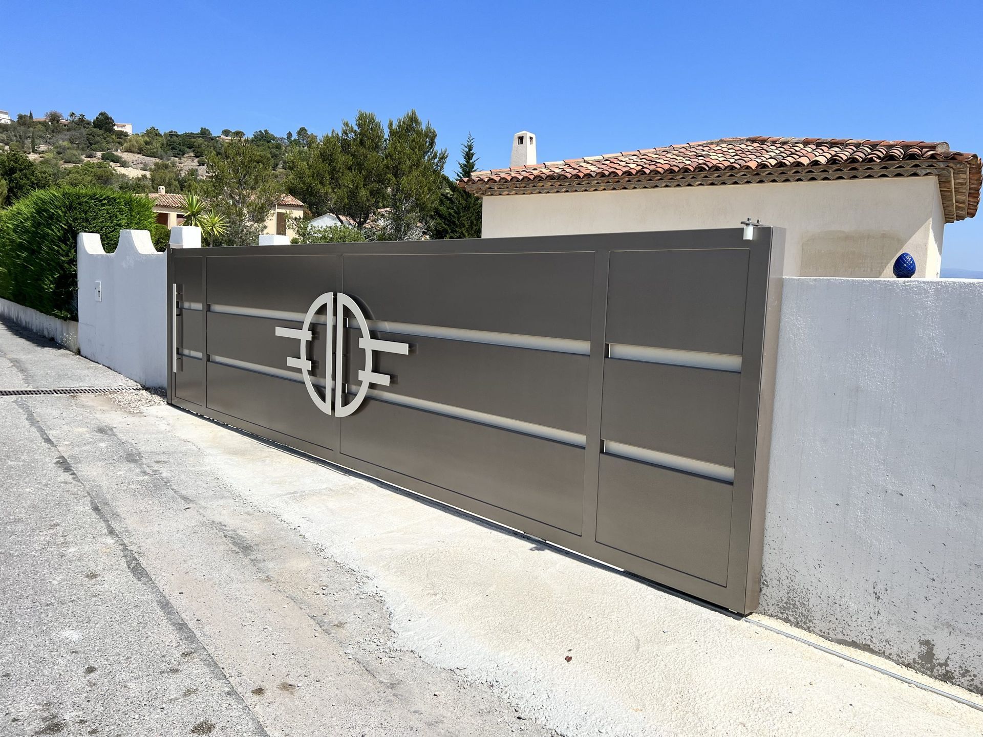 Portail d'allée moderne en métal gris, de forme circulaire, encastré dans un mur blanc en bordure de route et de maison.