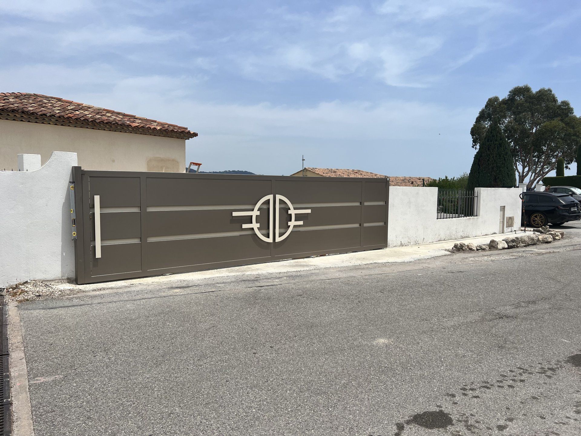Portail marron orné de motifs géométriques blancs devant une maison dans une rue calme
