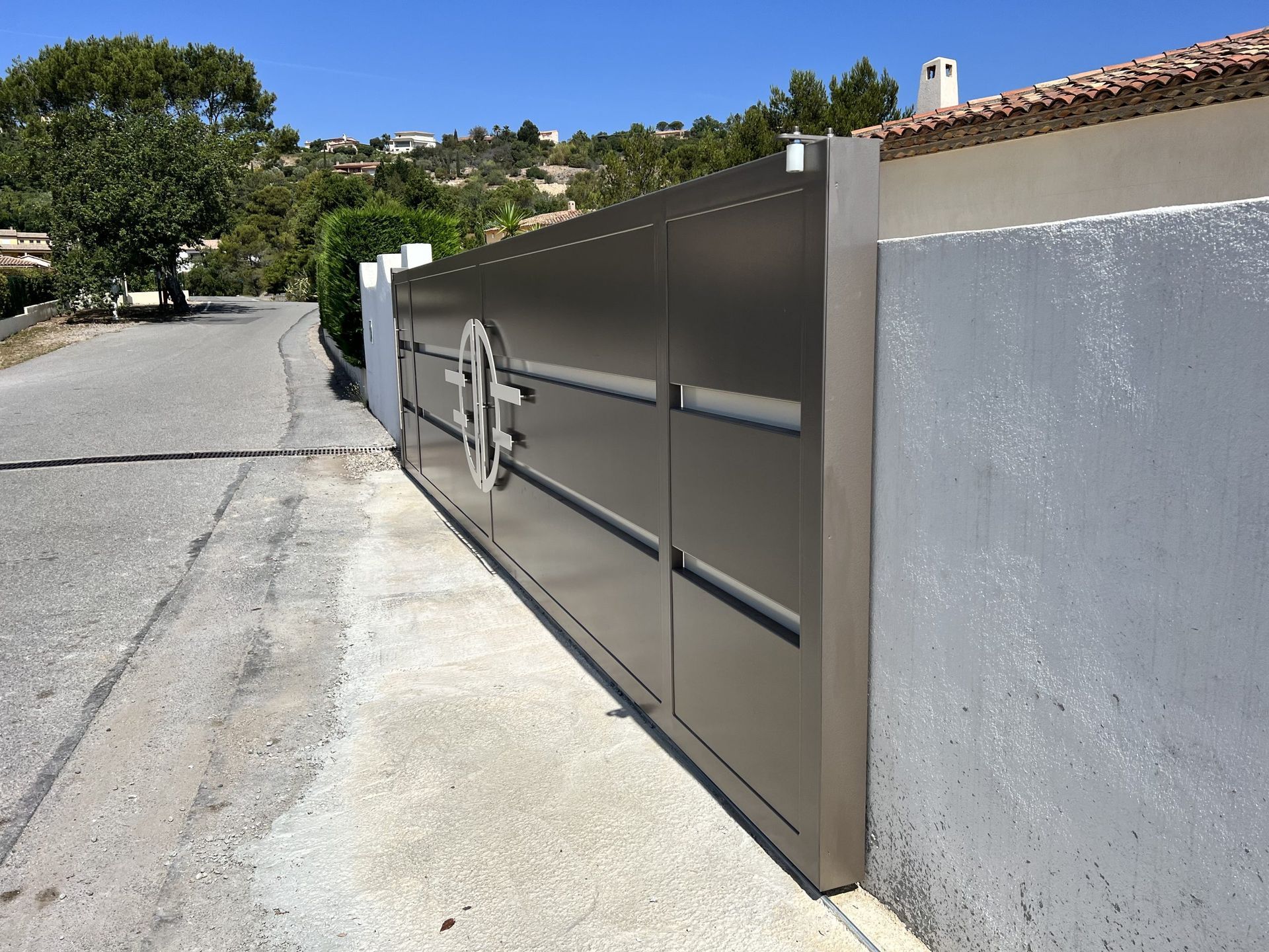 Portail d'allée moderne en métal, adossé à un mur blanc dans une rue résidentielle en pente.