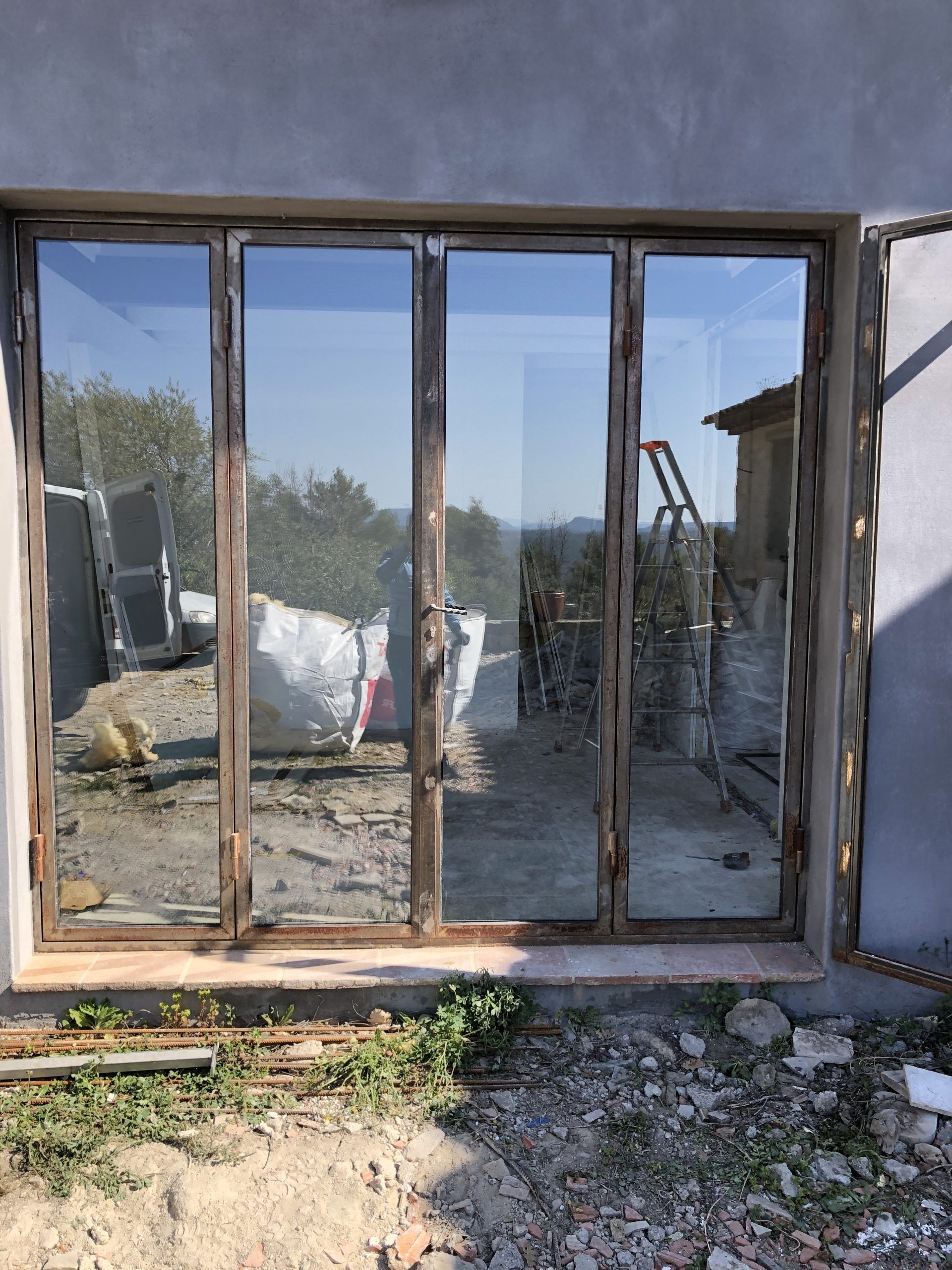 Porte coulissante en verre endommagée sur un mur en béton, donnant sur un espace extérieur poussiéreux.