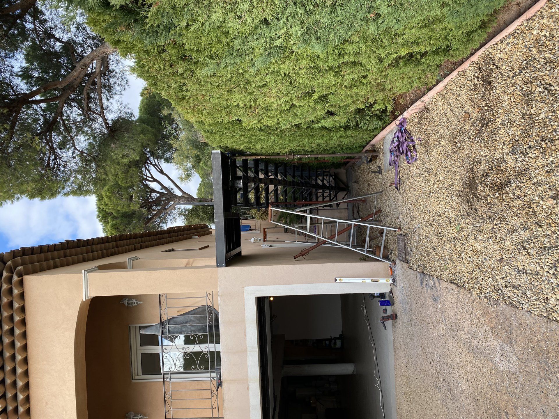 Entrée de maison avec pergola, allée de gravier et haies par une journée ensoleillée