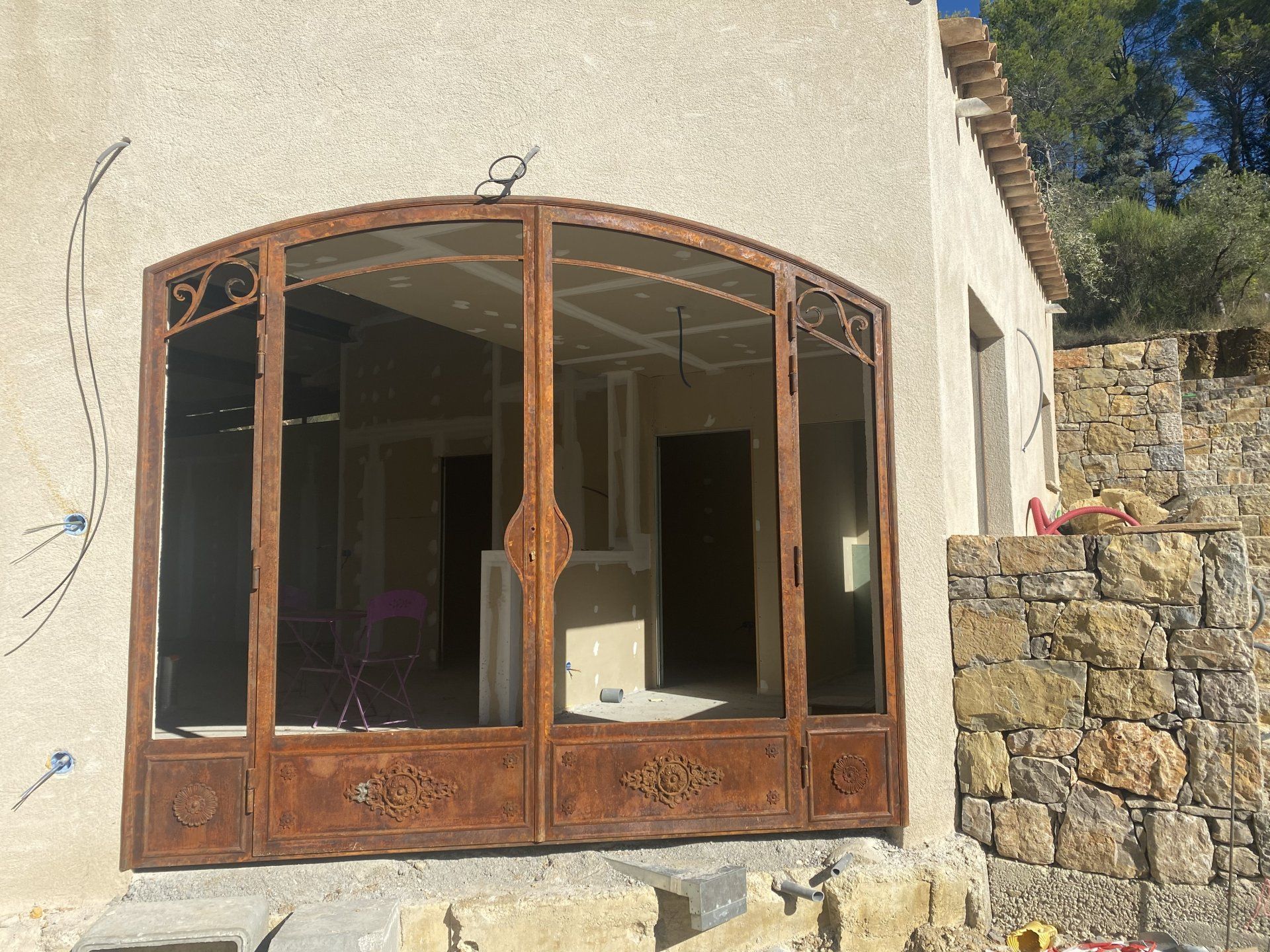 Portes cintrées en bois et en verre sur un bâtiment en stuc, à côté d'un mur de pierre et sous un ciel bleu.