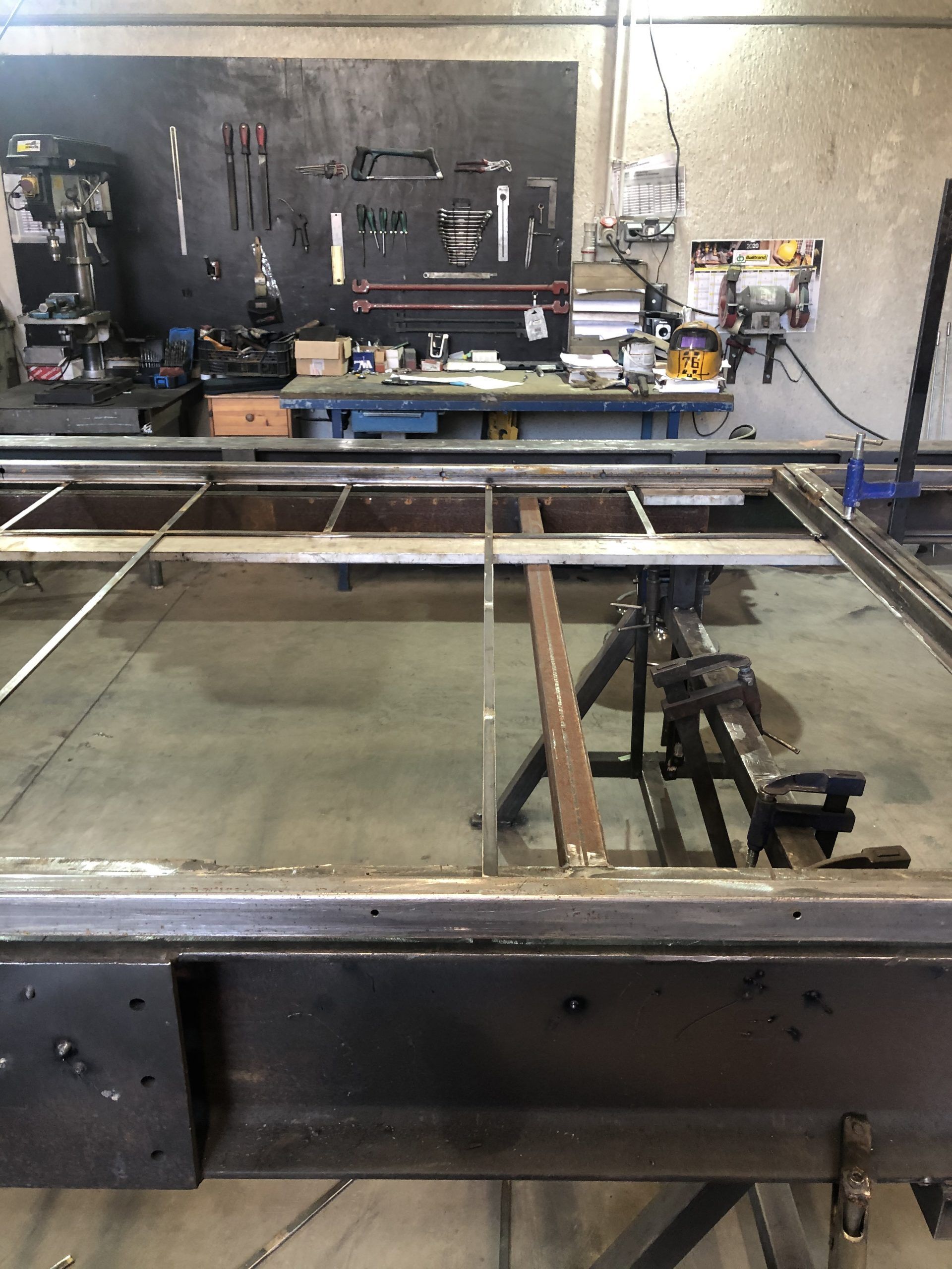 Atelier industriel avec une structure métallique et des machines sur un établi, vu au-dessus d'un bassin d'eau réfléchissant.