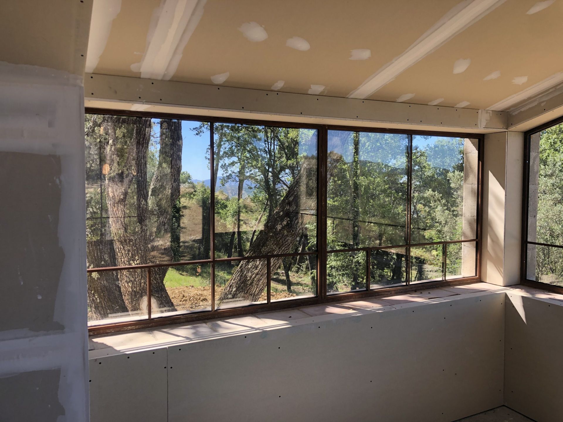 Intérieur lumineux d'une pièce avec de grandes fenêtres moustiquaires donnant sur les arbres et le feuillage.