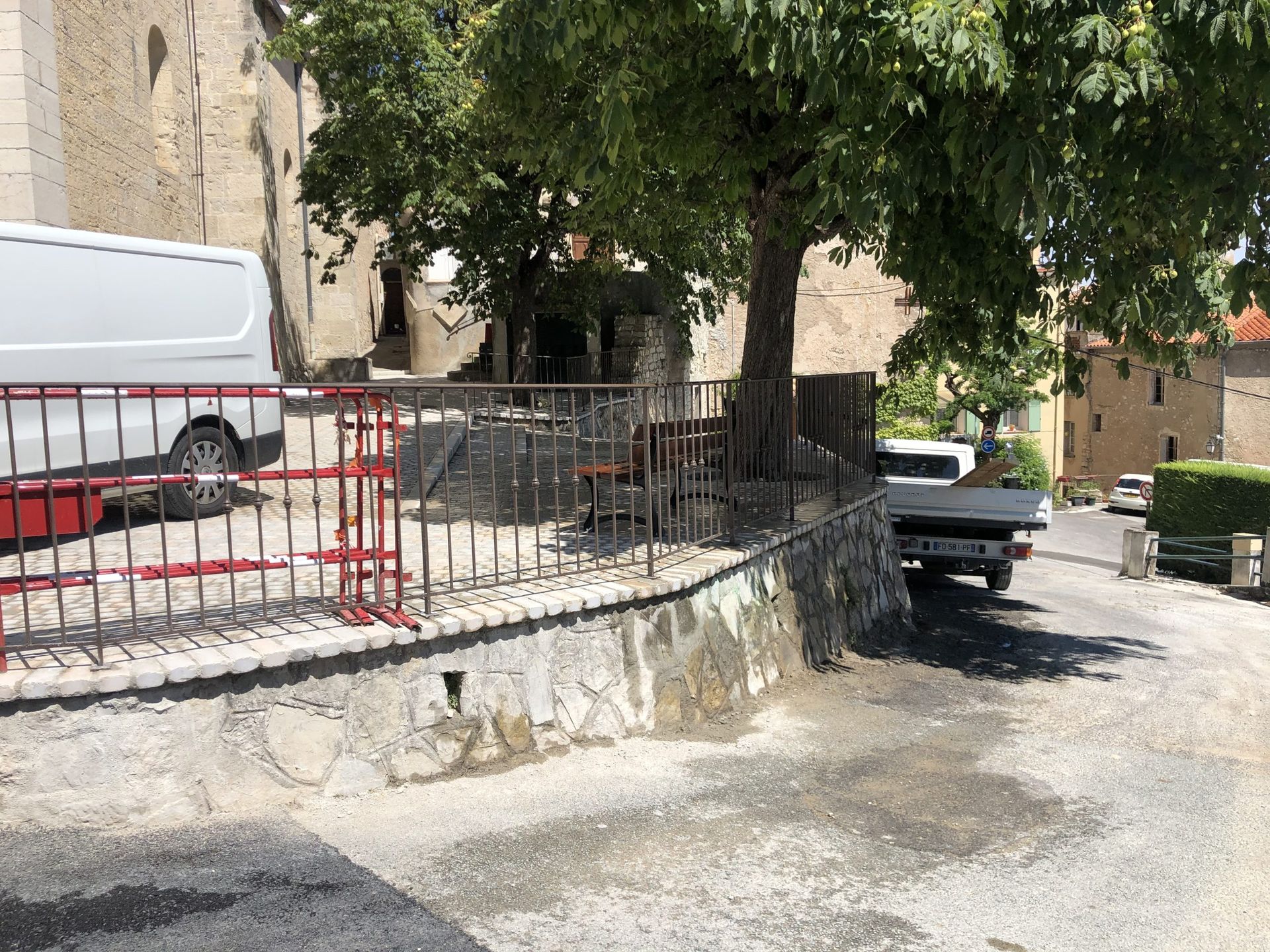 Cour intérieure tranquille avec mur en pierre, arbres, camionnette garée et voiture garée le long d'un chemin de gravier