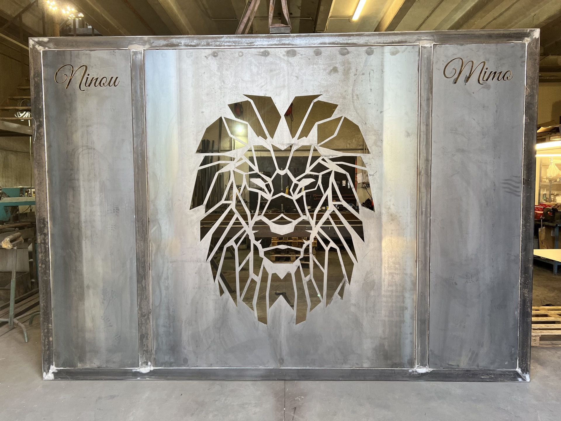 Grand panneau mural en métal argenté orné d'un motif de tête de lion découpée au centre.