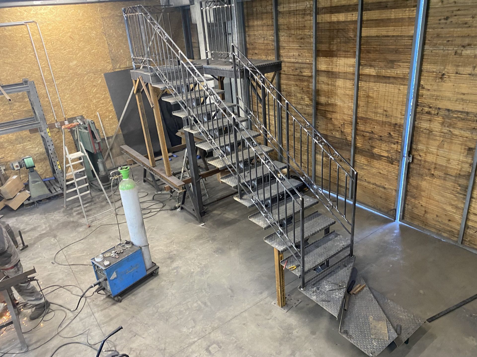 Escalier industriel avec rambardes métalliques dans un entrepôt, à côté d'une échelle et de produits de nettoyage sur un sol en béton