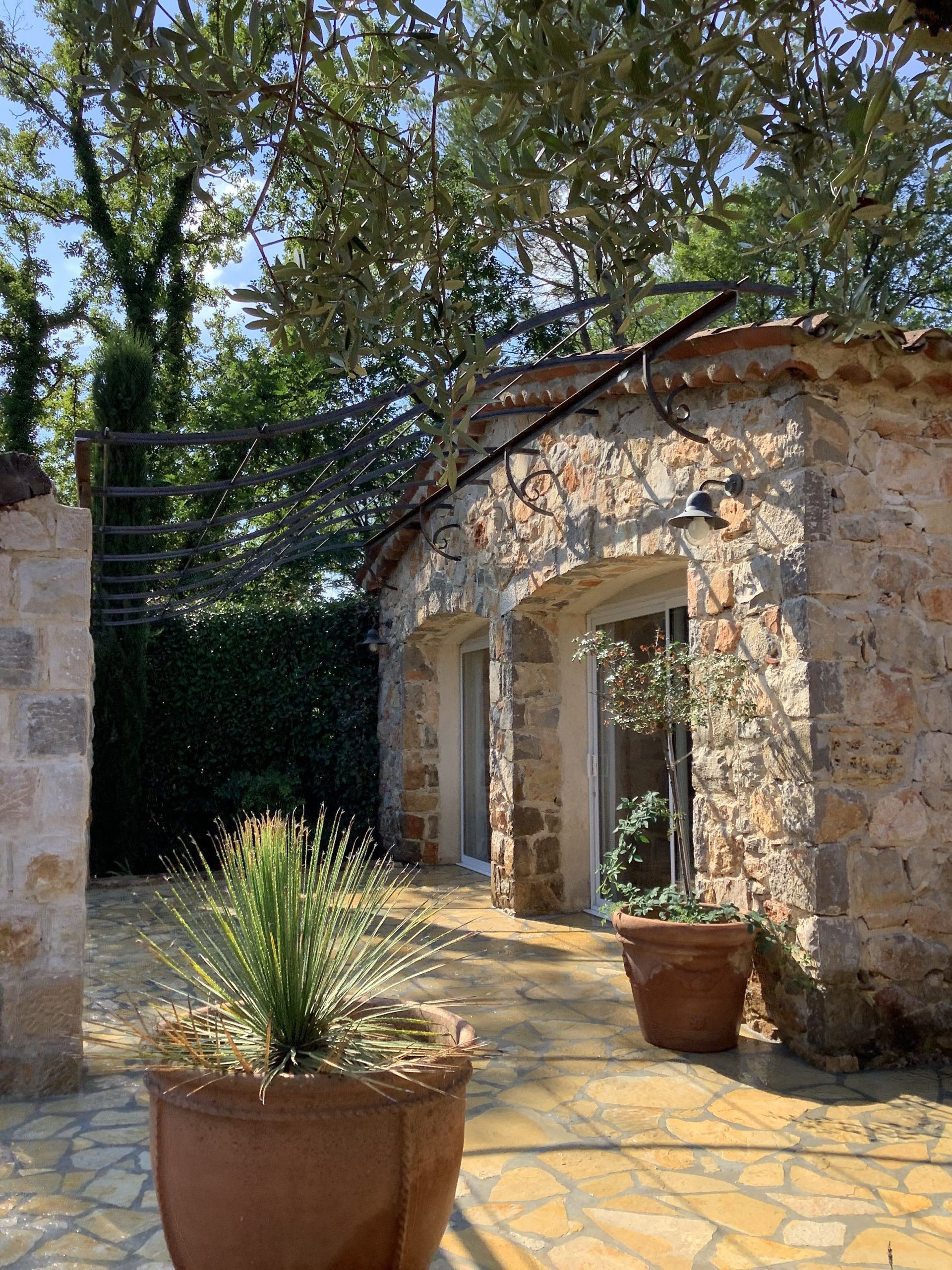 Cour en pierre avec des plantes en pot à côté d'un bâtiment rustique et d'arbres au-dessus