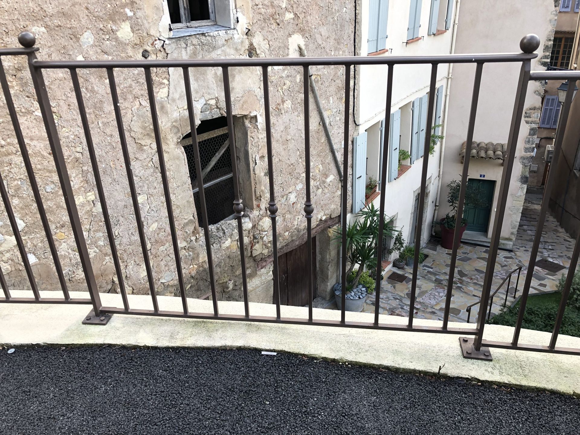 Rambarde de balcon donnant sur une ancienne cour en pierre avec des fenêtres et un petit arbre