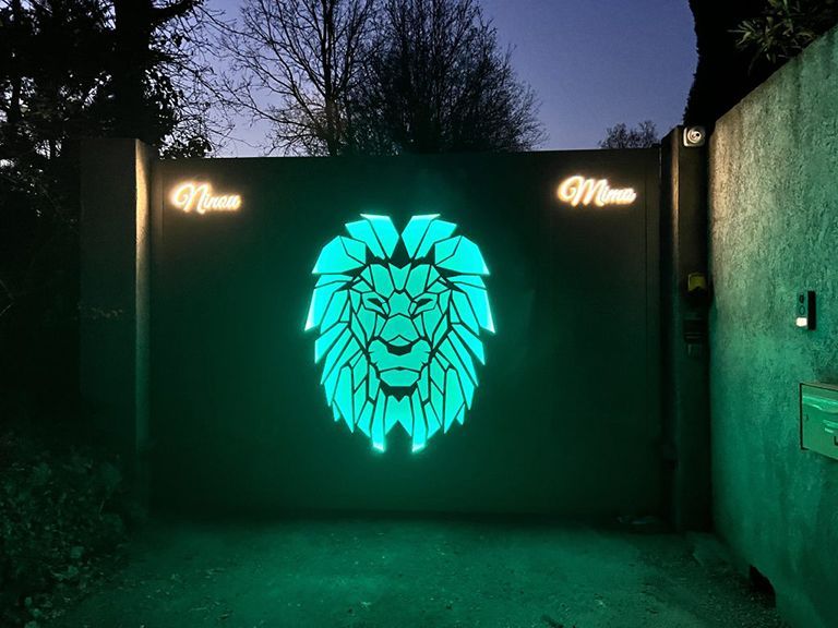 Une fresque murale de lion en néon illumine un portail sombre la nuit, avec une lumière verte et des arbres en arrière-plan.