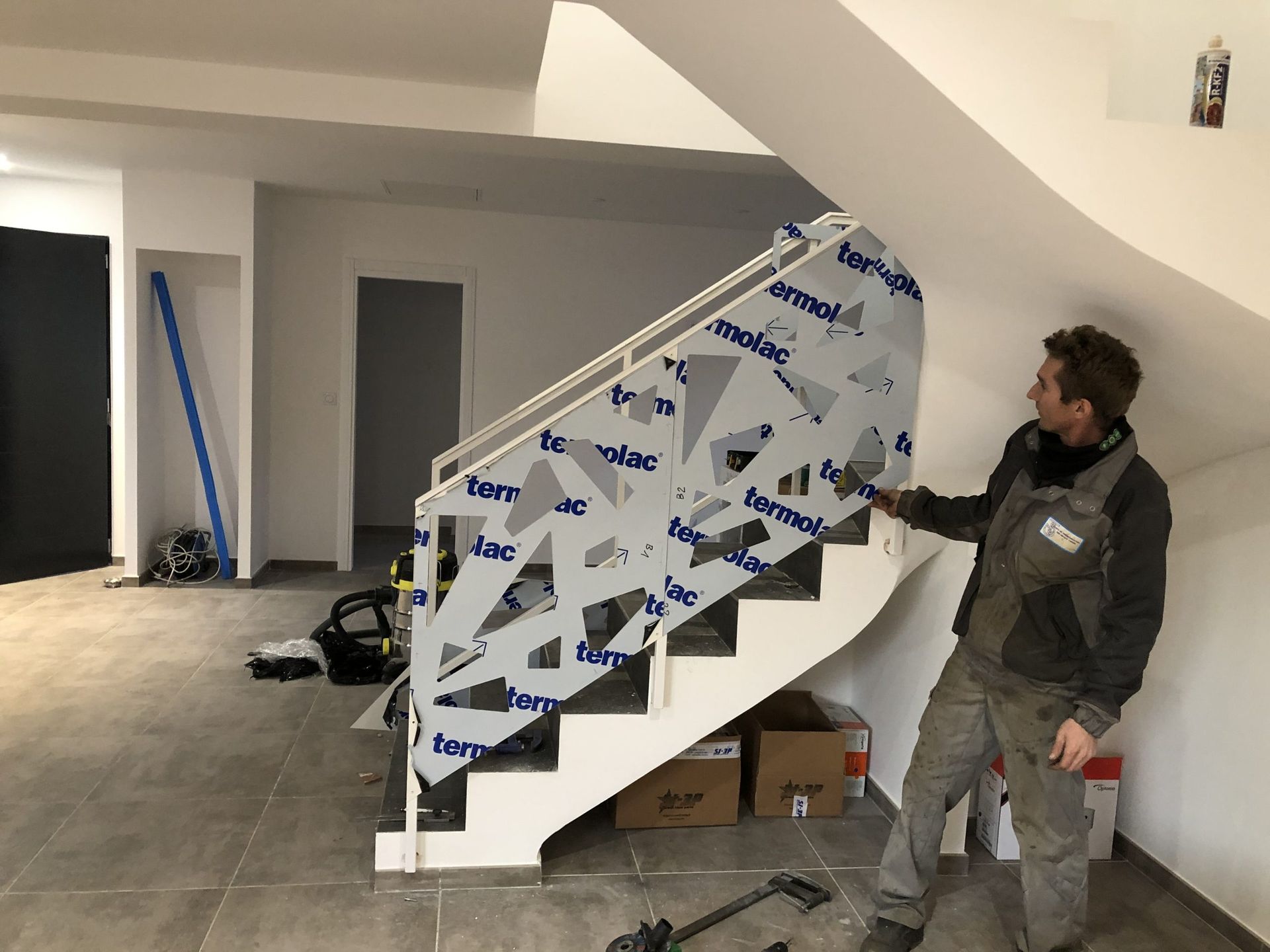 Un homme se tient debout près d'un escalier recouvert d'une bâche de protection imprimée à l'intérieur d'une pièce partiellement terminée.