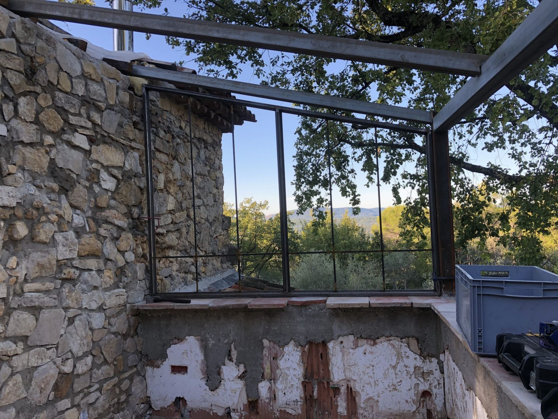 Ruines d'un patio en pierre avec une pergola à structure métallique, un muret et des arbres surplombant une vallée lointaine