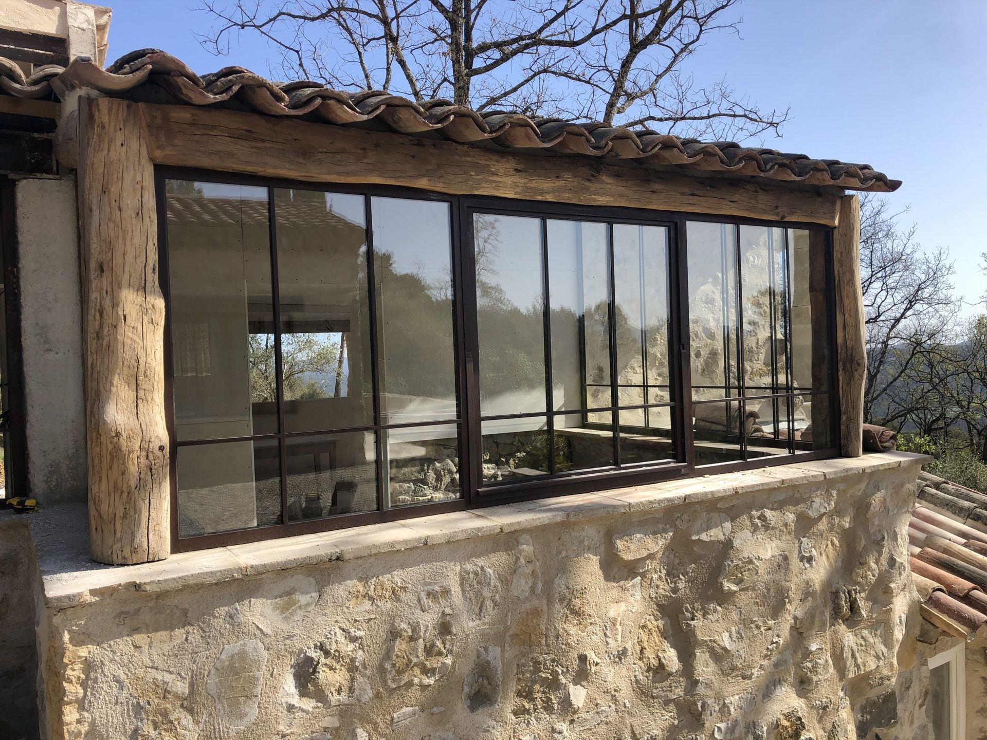 Maison rustique en pierre avec de grandes baies vitrées et un toit de tuiles à flanc de colline