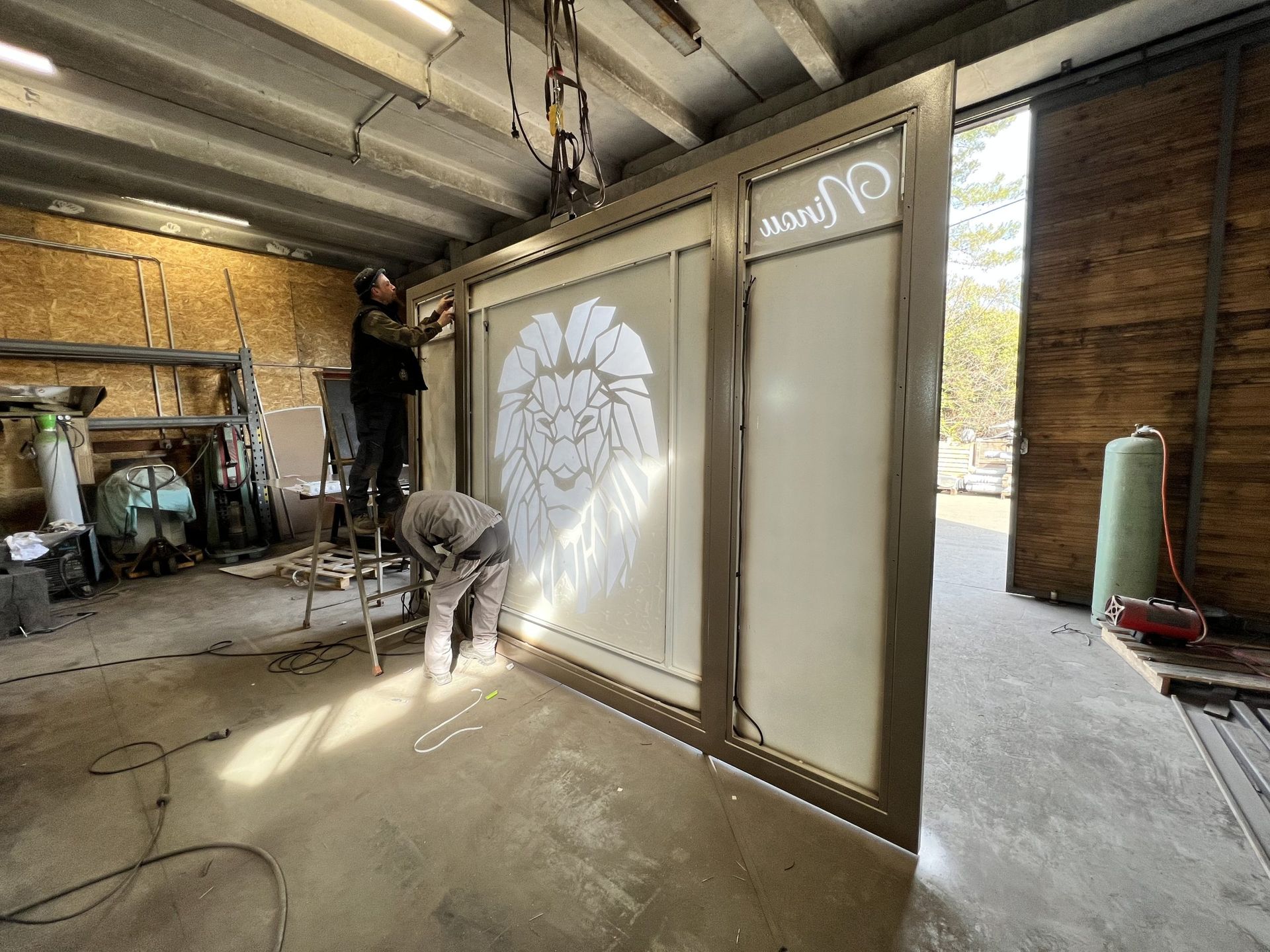 Intérieur d'atelier avec une porte coulissante dépolie, la lumière du soleil inondant l'espace, et des outils et équipements disposés un peu partout.