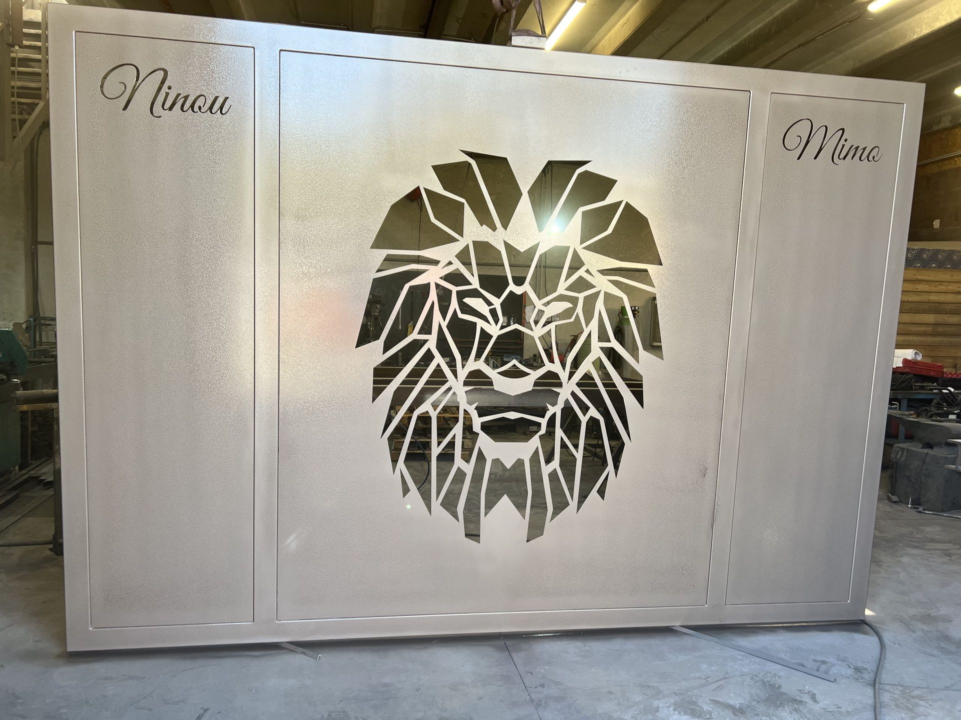 Panneau métallique argenté orné d'une tête de lion découpée au laser dans un coin.
