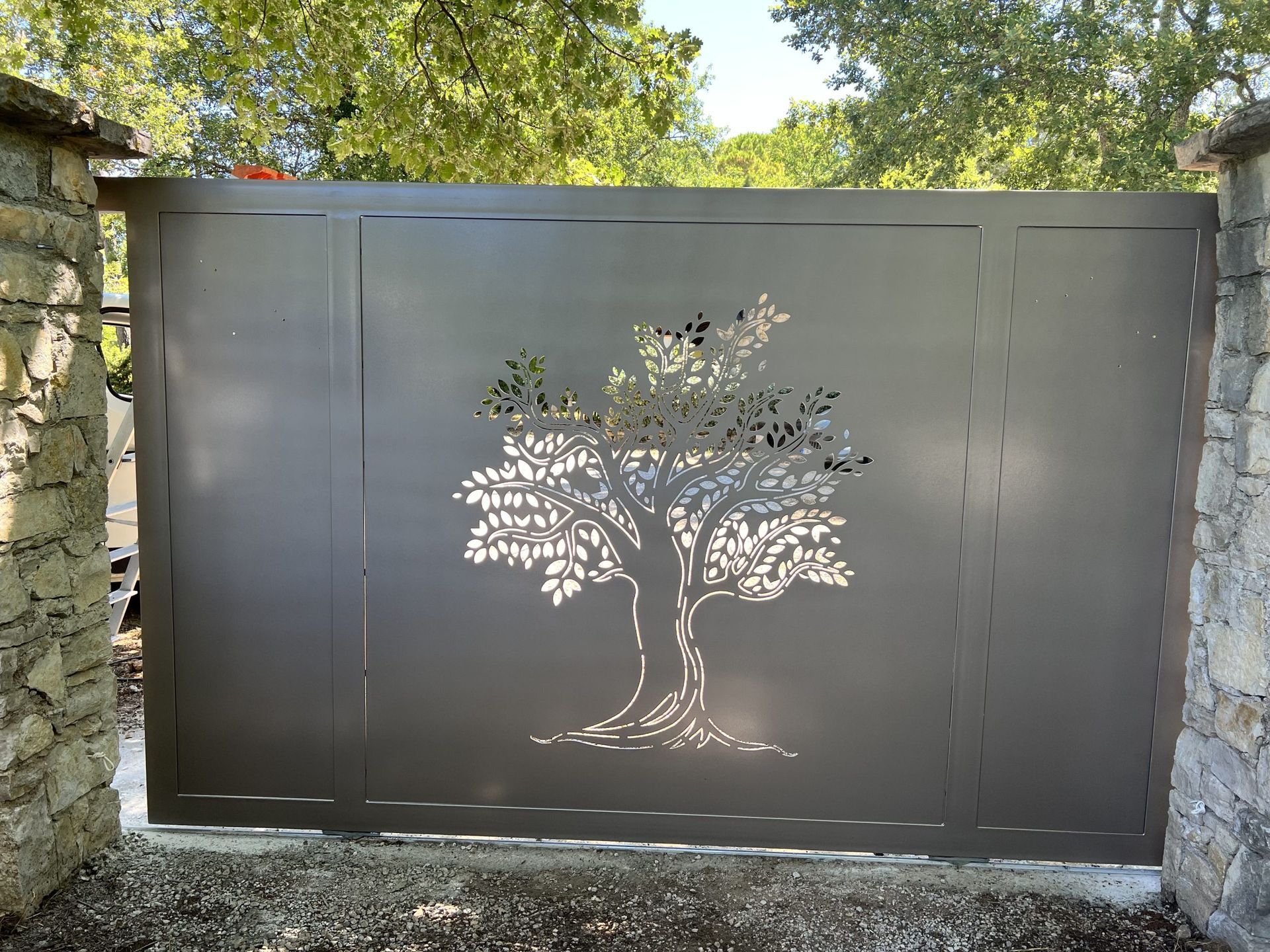 Portail en métal gris avec un motif d'arbre ajouré et la lumière du soleil filtrant à travers
