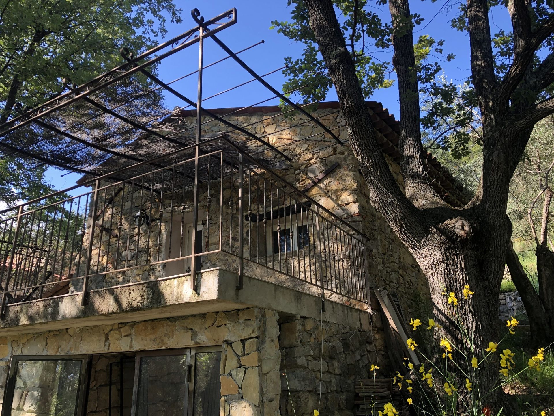 Maison en pierre en construction avec échafaudages en bambou et un grand arbre devant