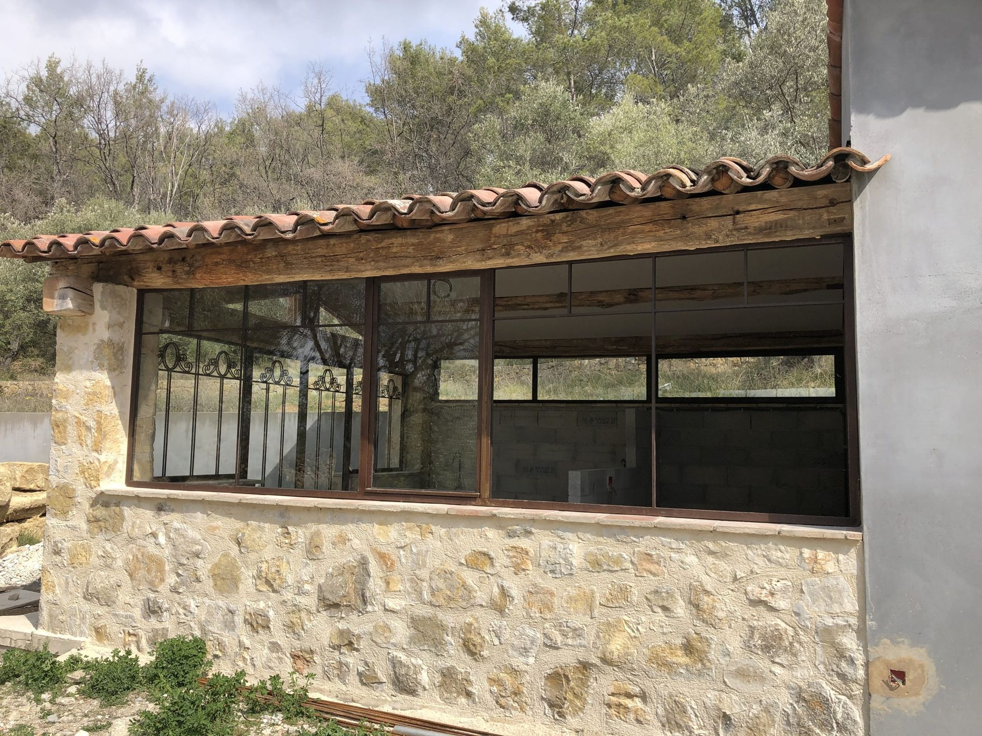 Bâtiment rustique en pierre avec fenêtres ouvertes et toit de tuiles au milieu des arbres