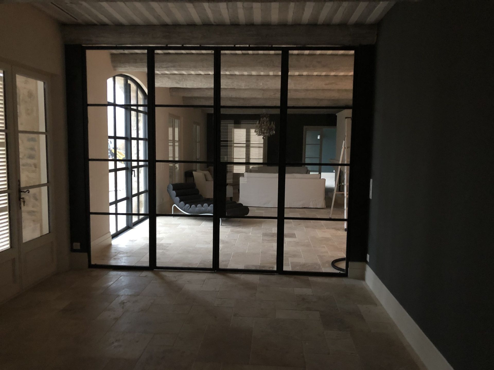 Pièce vide aux murs sombres, au sol carrelé et aux portes vitrées s'ouvrant sur un espace intérieur plus lumineux.