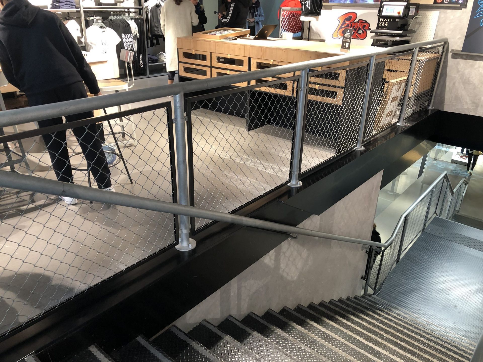 Cage d'escalier intérieure avec rampes en métal noir, paroi vitrée et une personne debout près du palier supérieur.