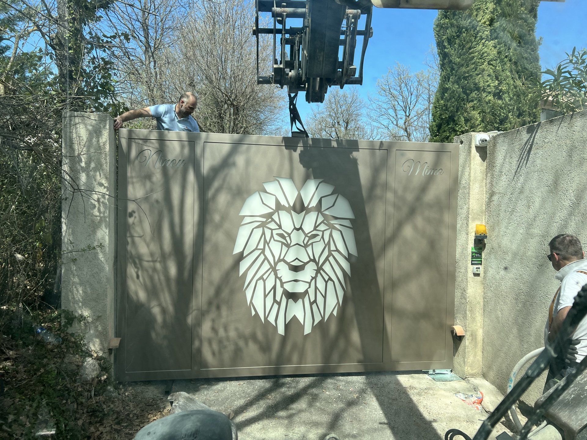 Une personne peint une grande fresque de lion sur un portail beige à l'extérieur, avec un ascenseur au-dessus.