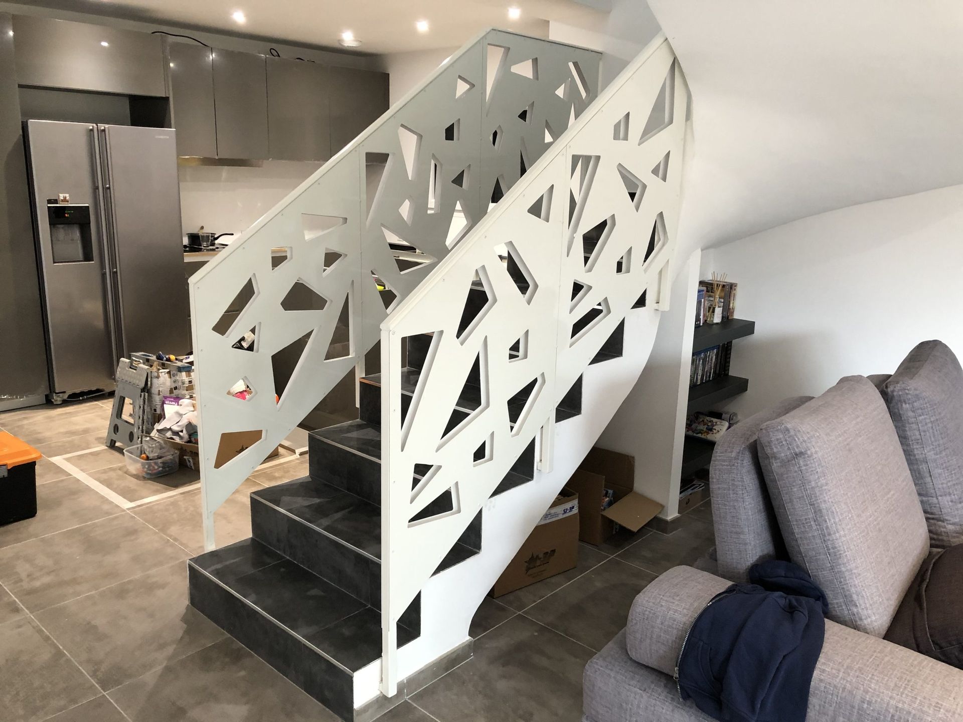 Cuisine et salon modernes avec escalier noir et rampe géométrique blanche à côté d'un canapé gris.