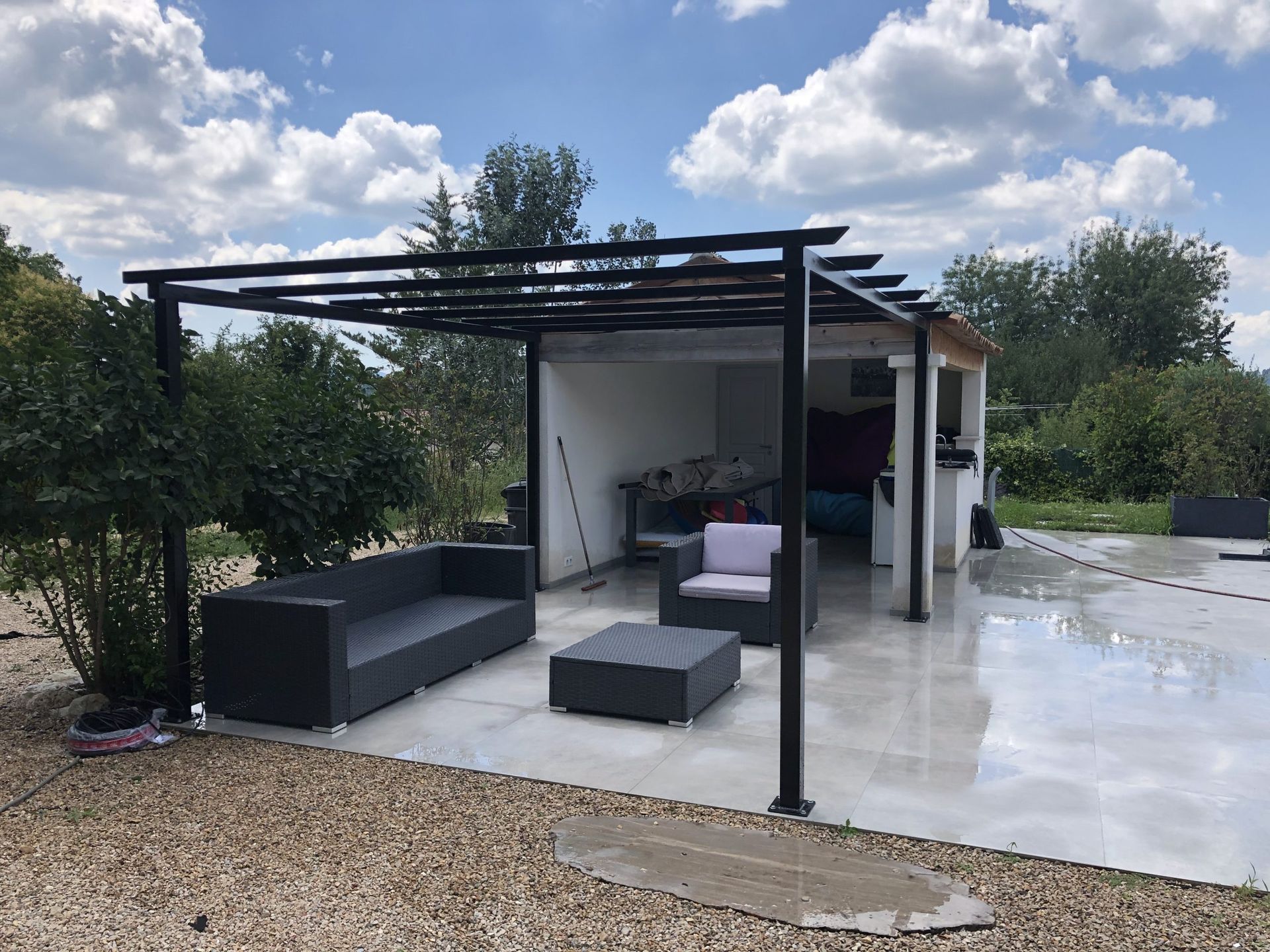 Patio moderne avec pergola noire, sièges d'extérieur, sol en béton blanc et vue sur le jardin