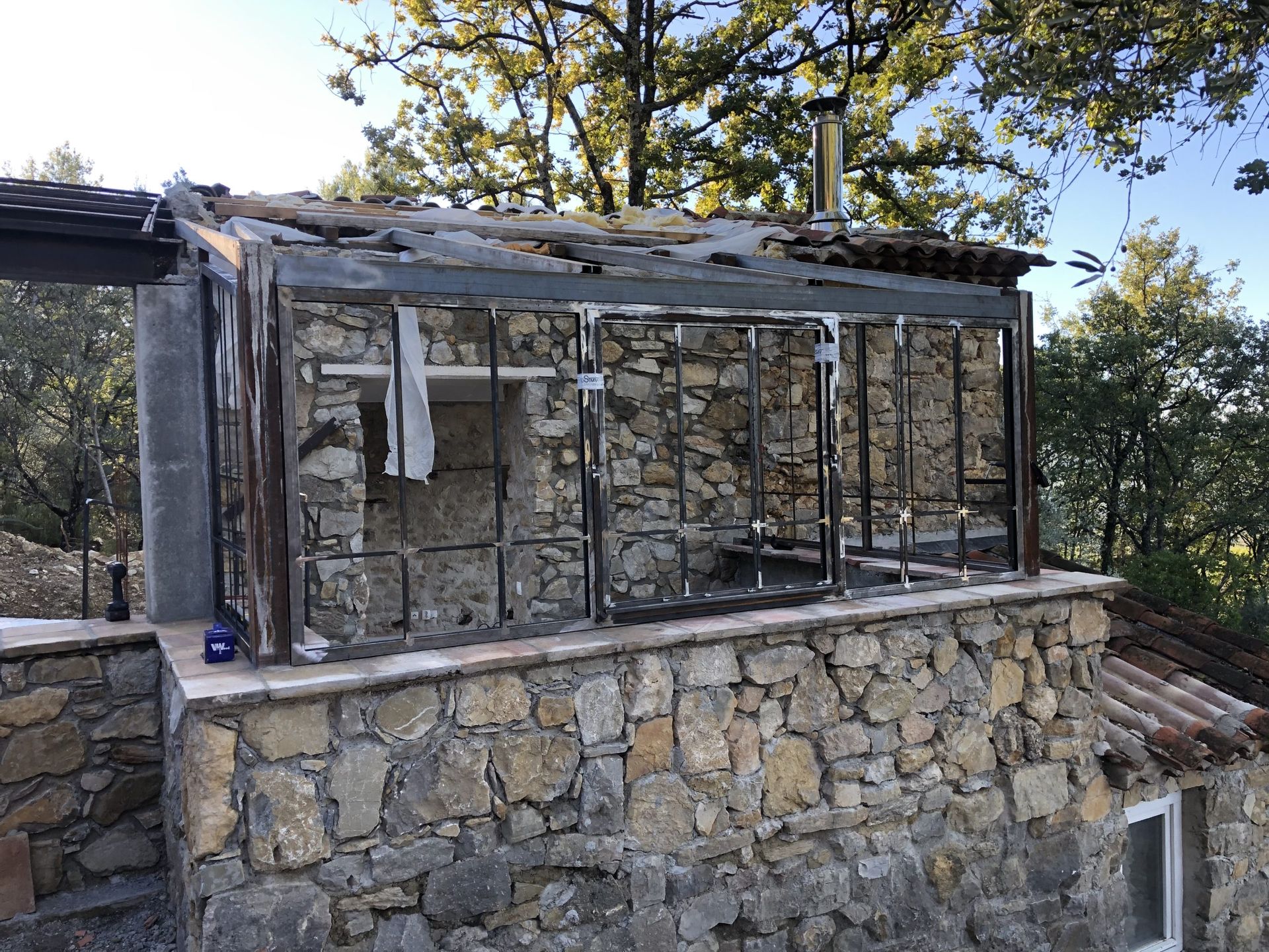 Serre en pierre à flanc de colline, avec une structure métallique et des panneaux de toit en verre