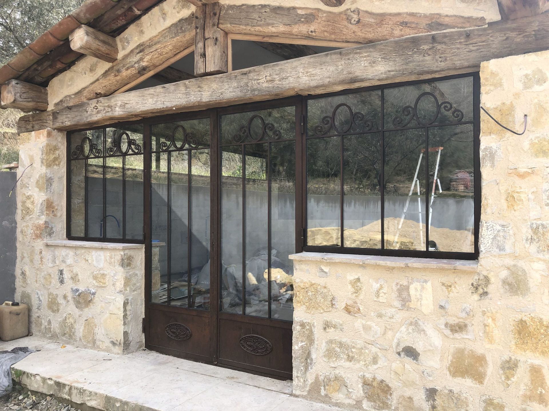 Entrée en pierre avec portail en métal noir et fenêtre sous un toit rustique en bois