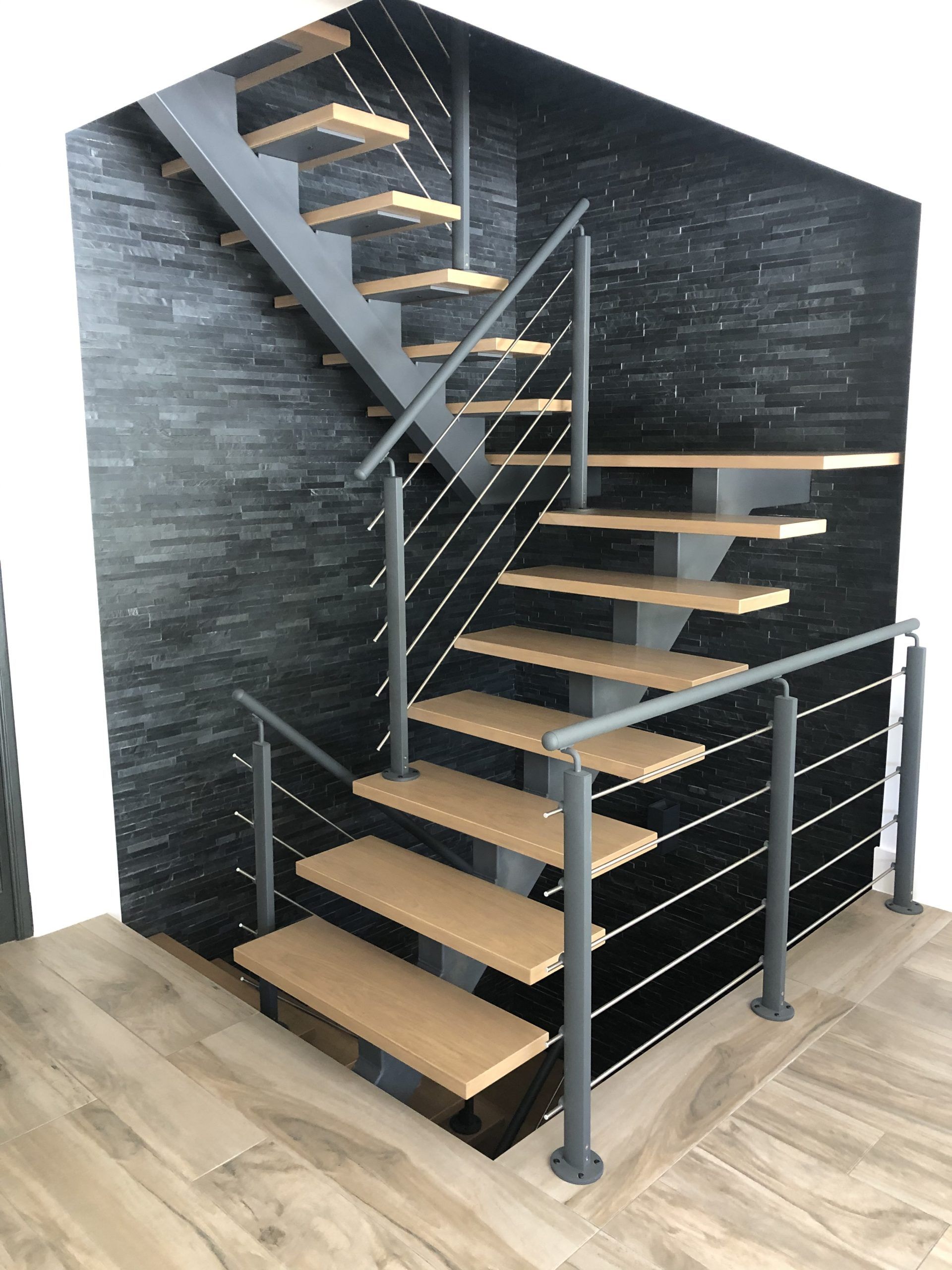 Escalier intérieur moderne avec marches en bois, rampe noire et mur d'accent en pierre sombre