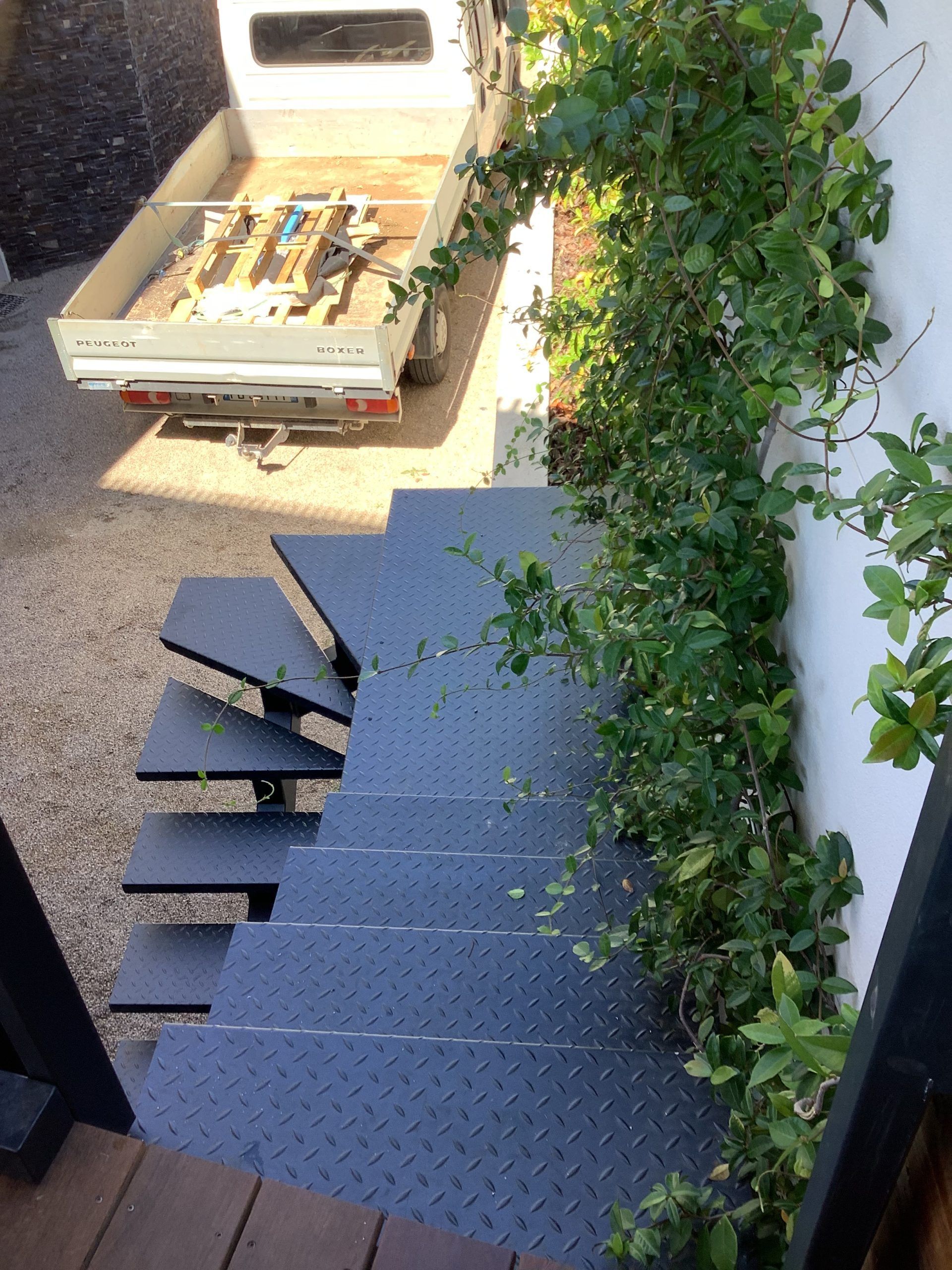 Escalier recouvert de moquette bleu-gris et agrémenté de verdure, à côté d'un camion blanc transportant une palette en bois en haut.